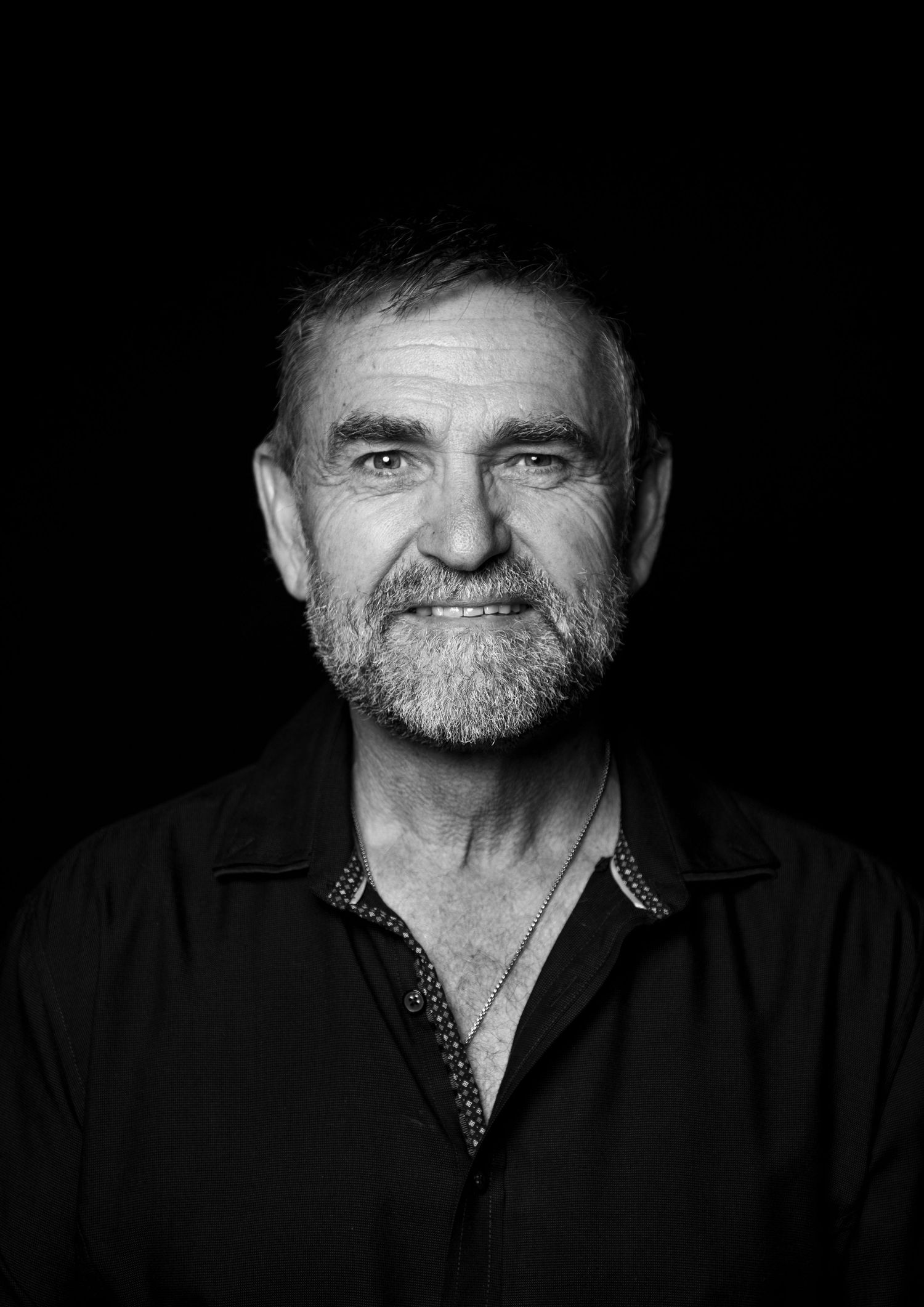 Black and white portrait of a smiling older man with short gray hair and beard wearing a dark shirt.