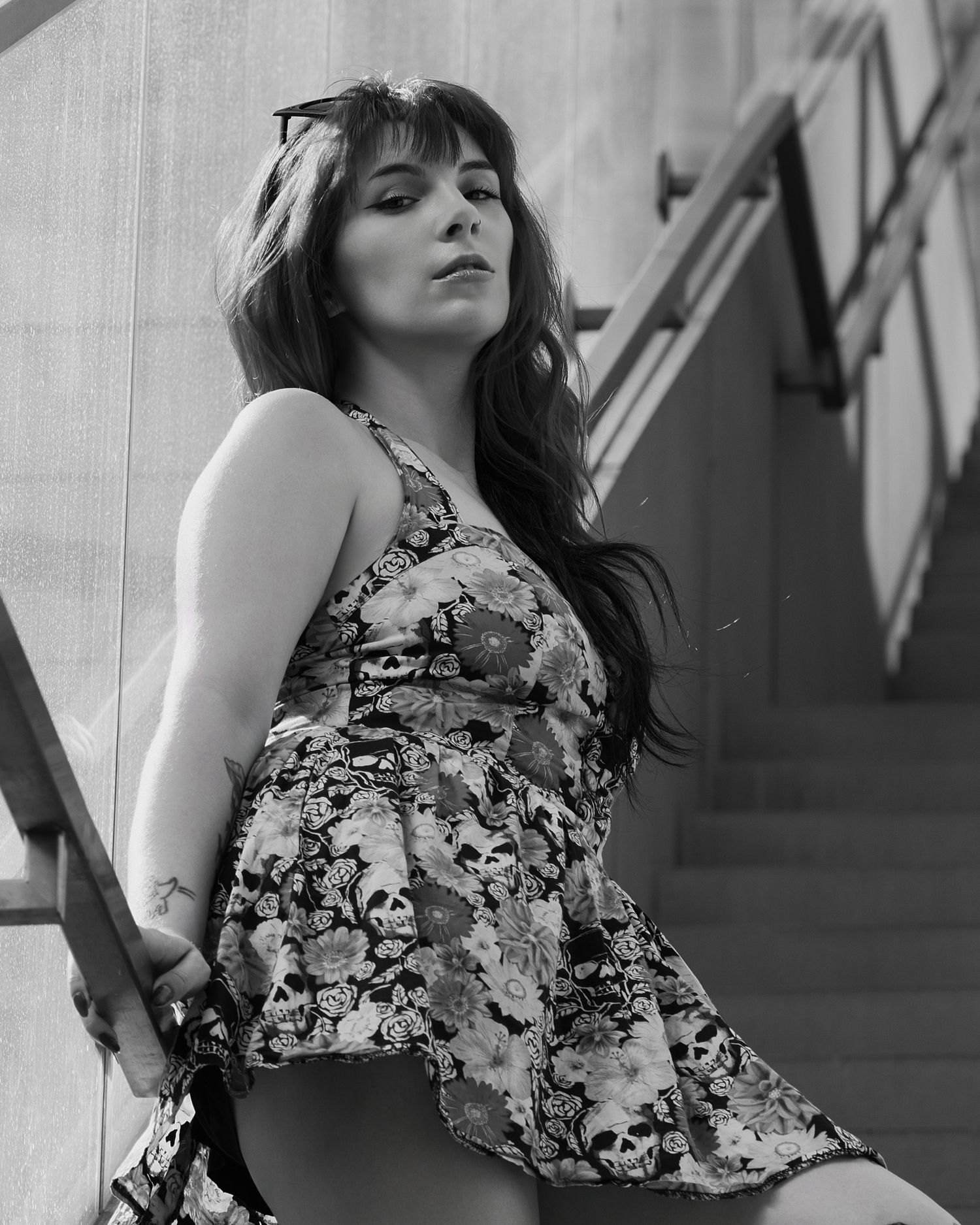 Black and white photo of a young woman in a floral skull dress posing on outdoor stairs.