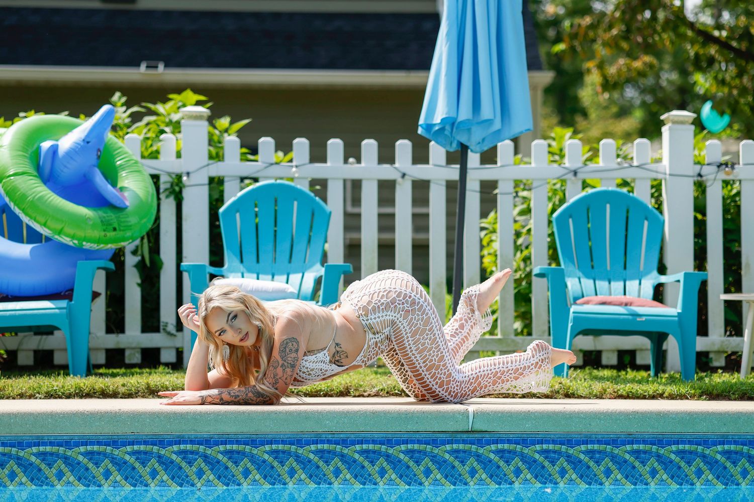 Woman in floral outfit posing by a blue pool with Adirondack chairs and a green inflatable float.
