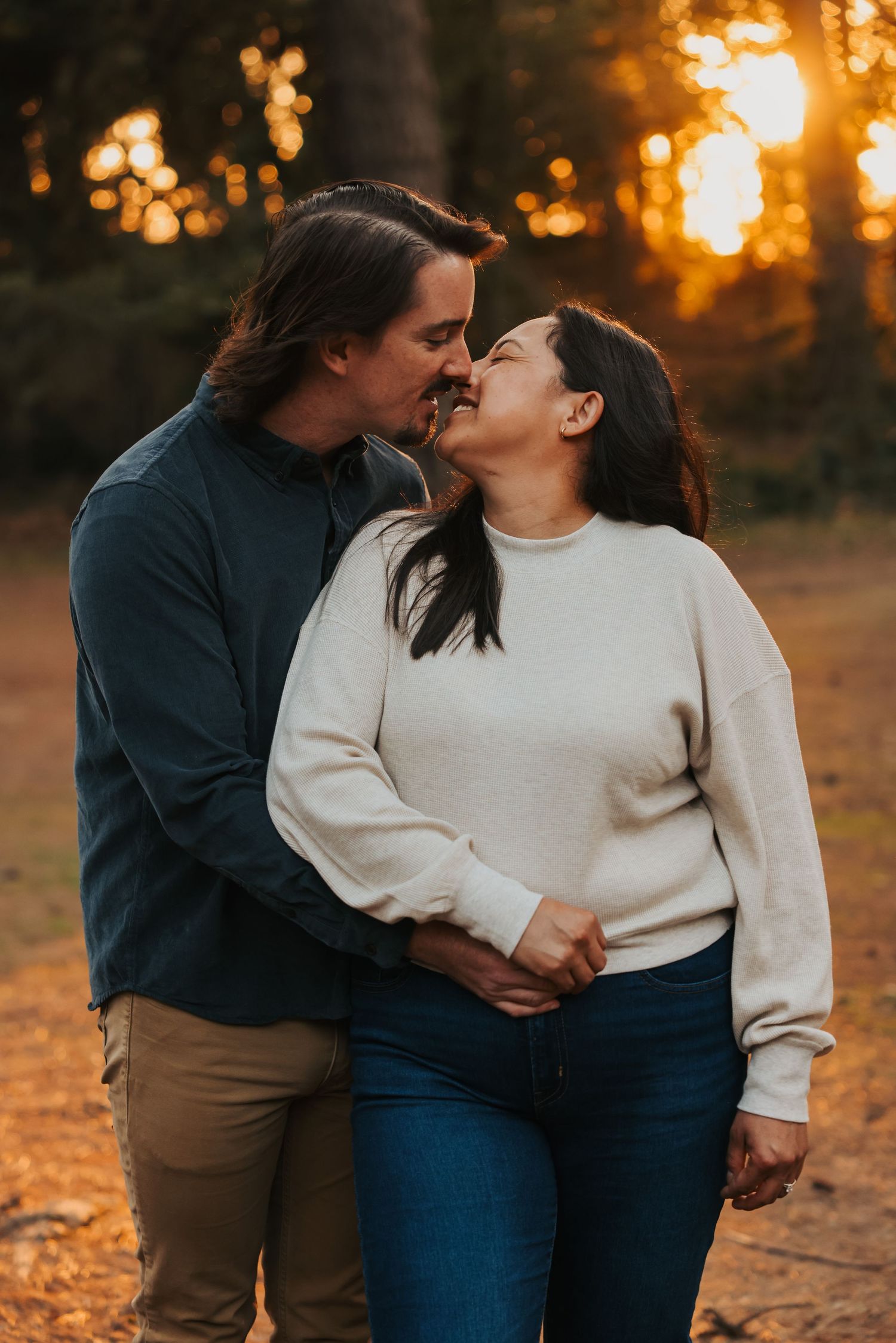 Romantic couple shares a kiss at sunset in an autumn forest, bathed in warm golden light.