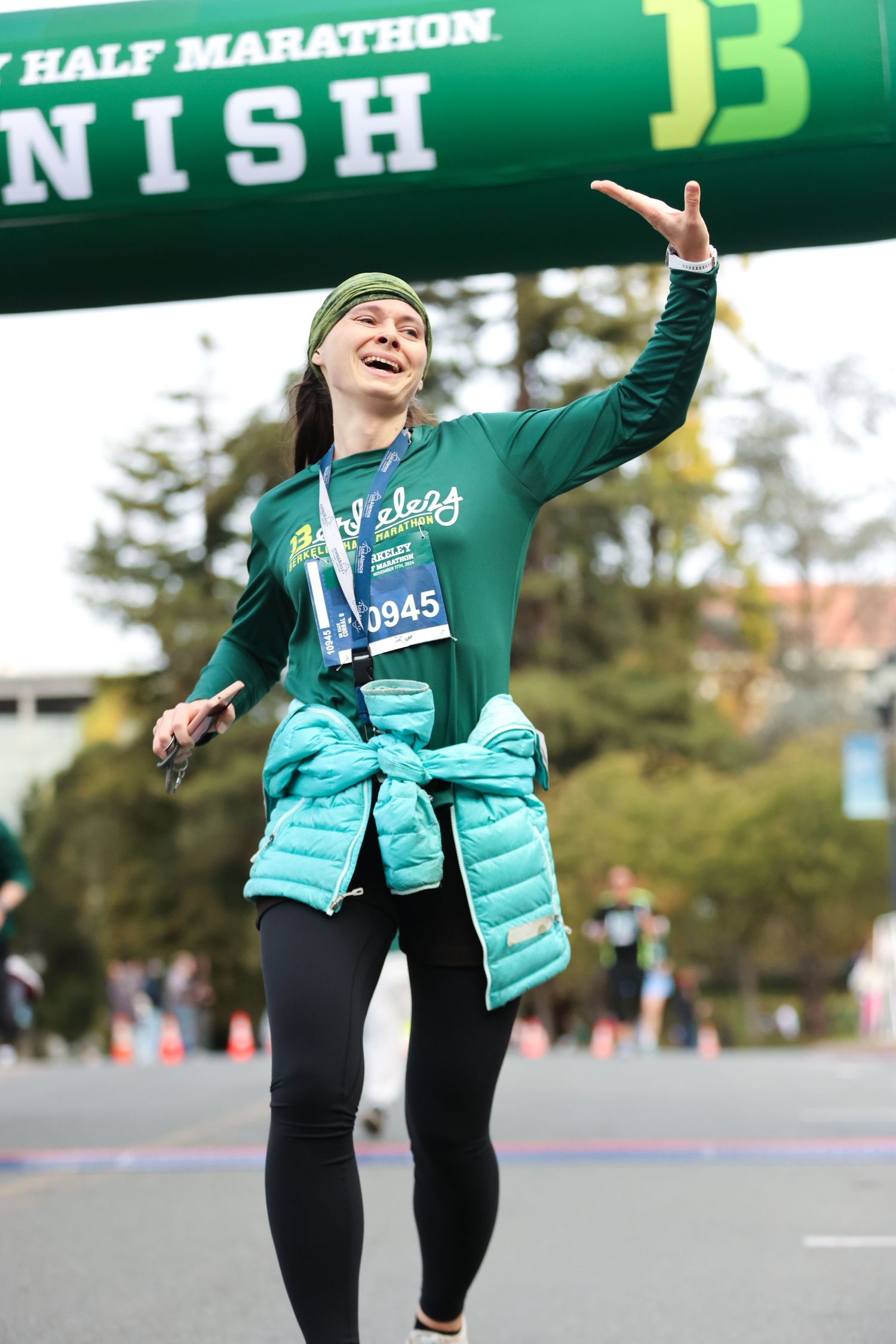 Emotional female runner celebrates crossing the half marathon finish line wearing a green Berkeley shirt.