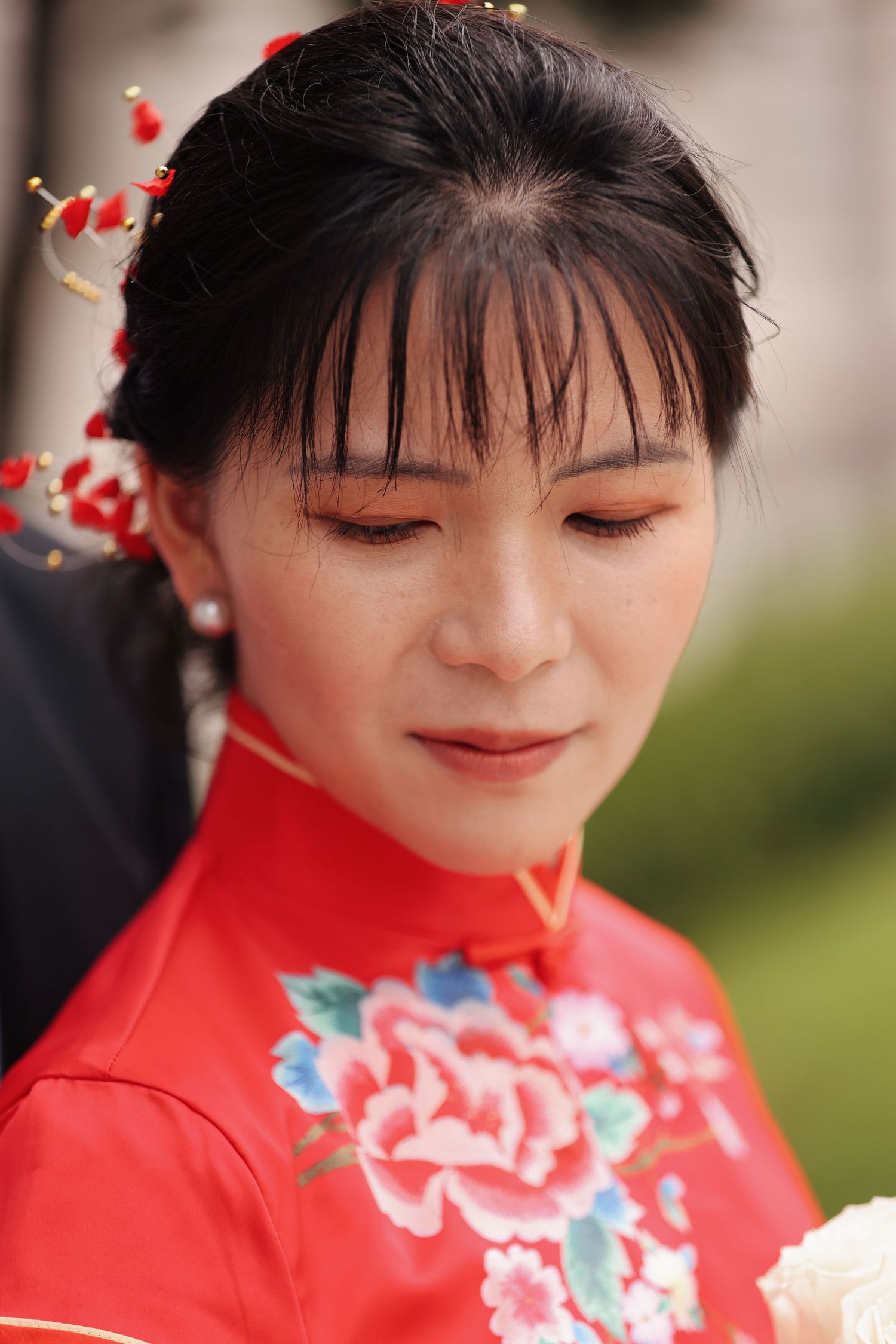 Close-up portrait of a bride in a red embroidered qipao with traditional red hair accessories.