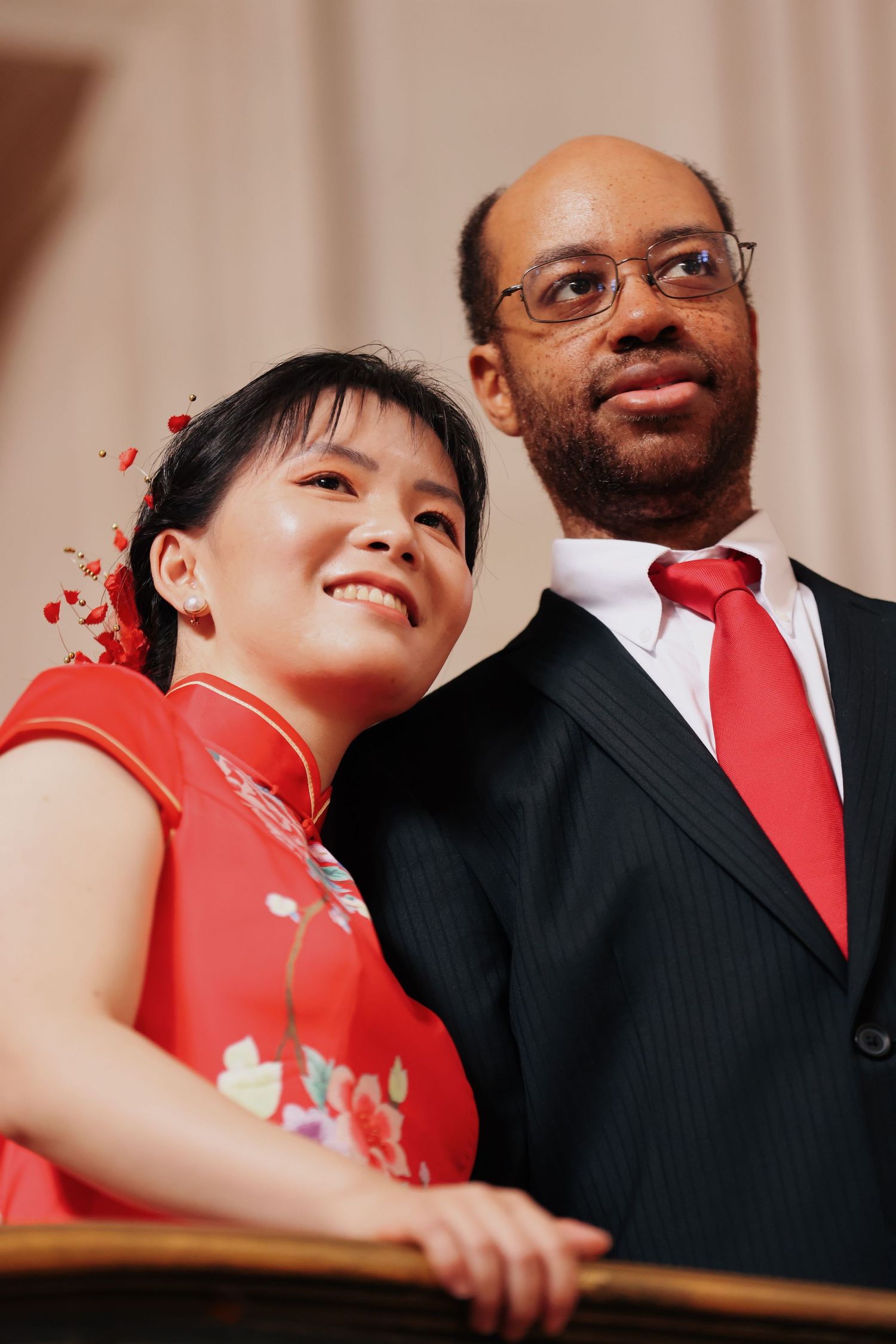 Interracial couple posing together, woman in red floral cheongsam and man in black suit with red tie.