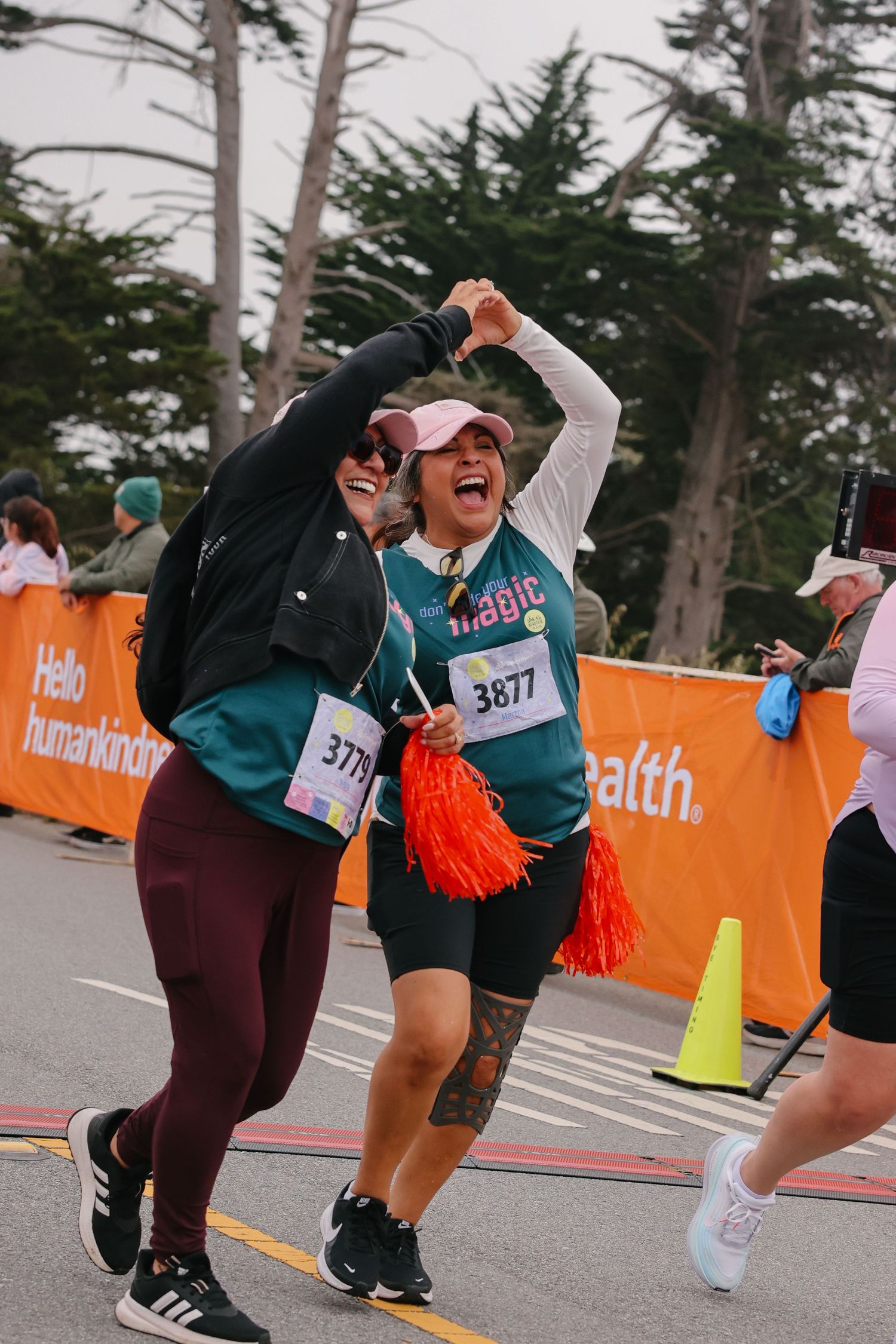 An excited woman wearing bib 3877 celebrates near the finish line of a running race.