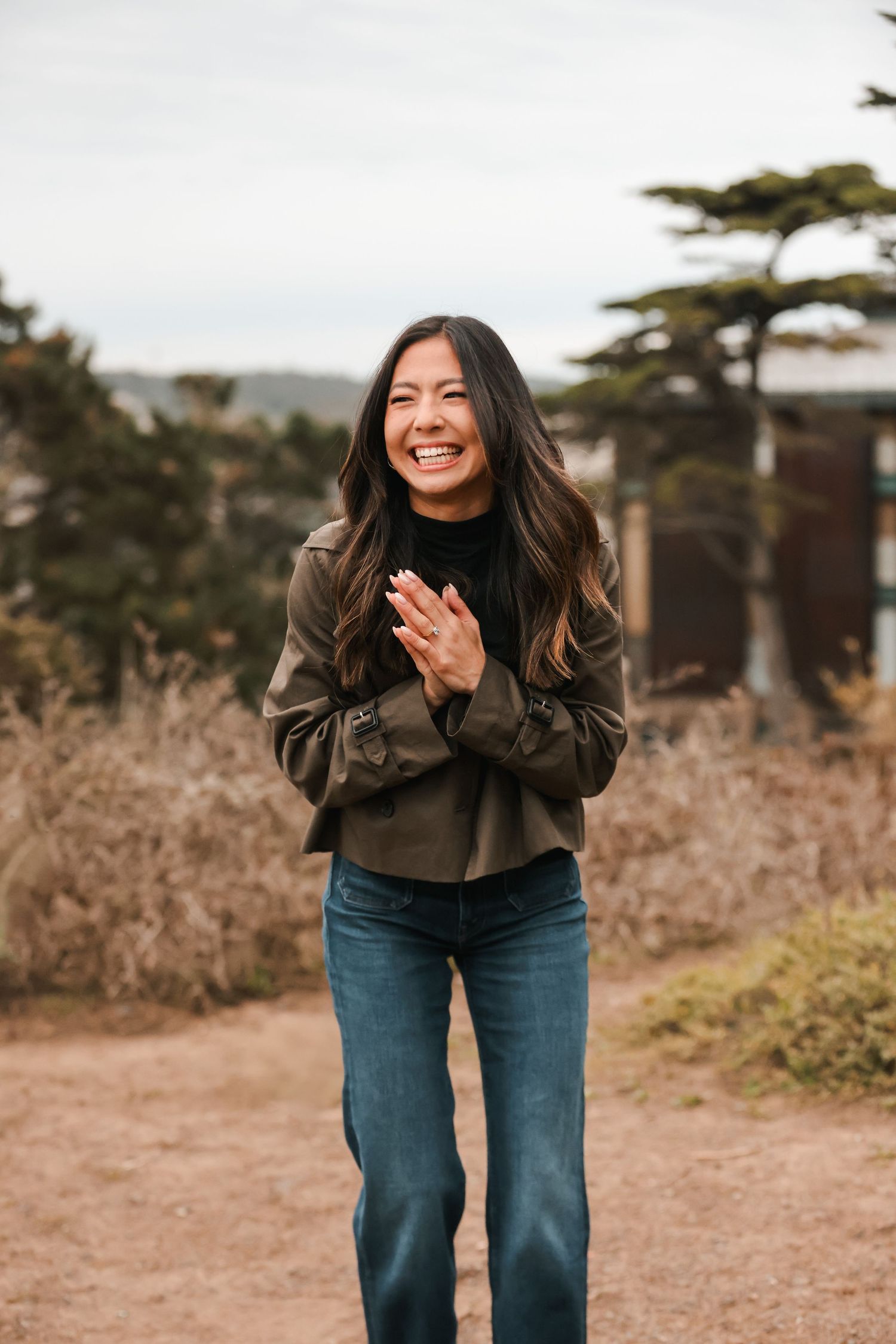 Joyful woman clasping hands together, laughing outdoors among dried natural grasses.