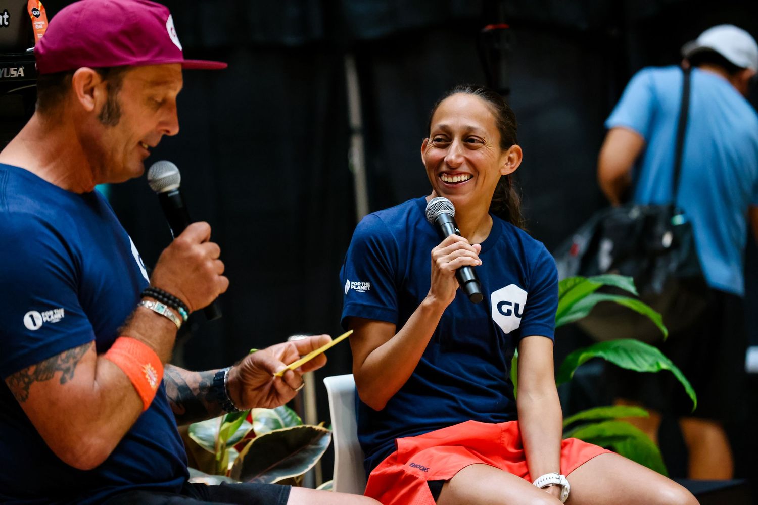 Two athletes share a laugh during a post-race interview at an outdoor running event.