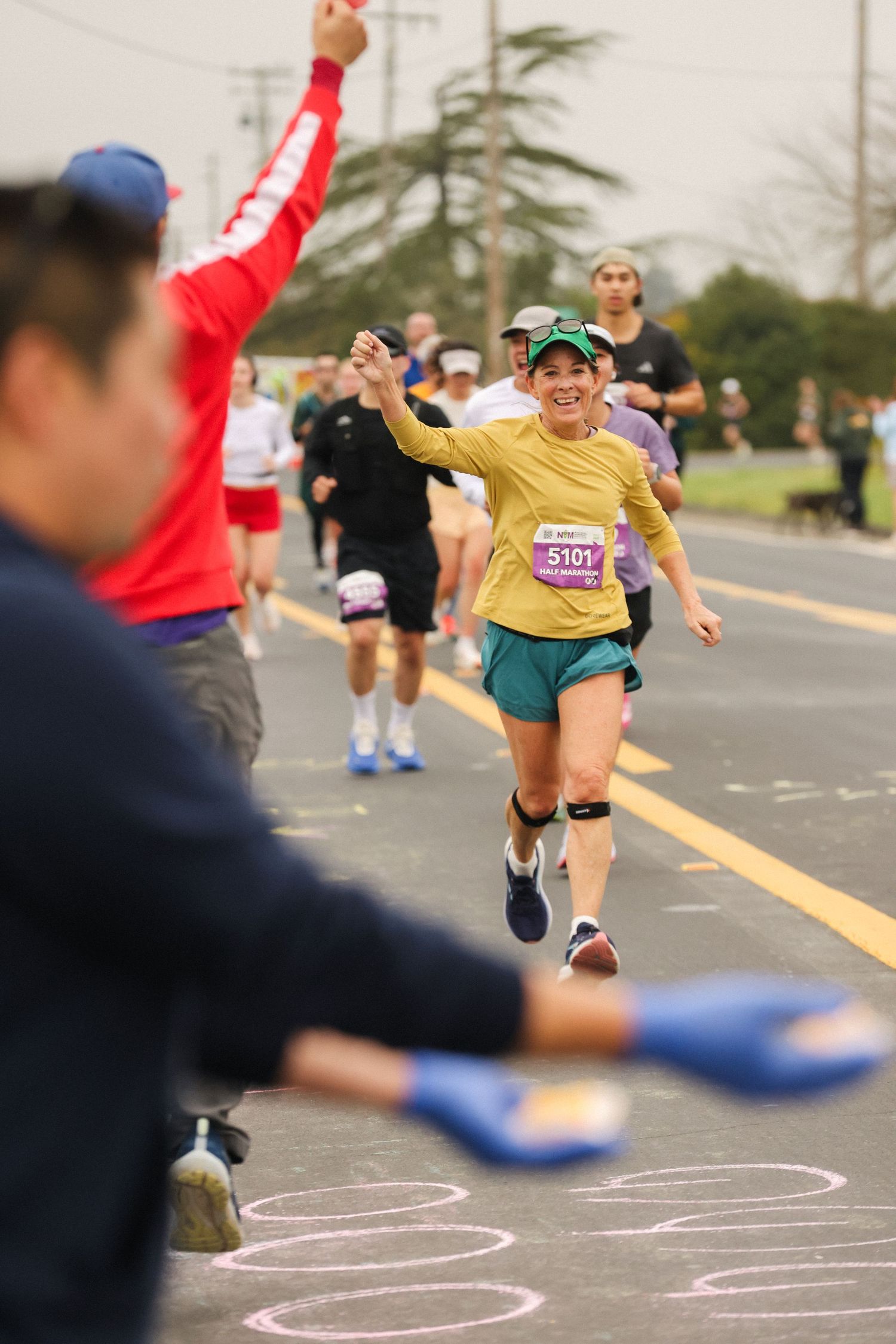 Smiling female runner in yellow shirt high-fives spectators during an outdoor road marathon race.