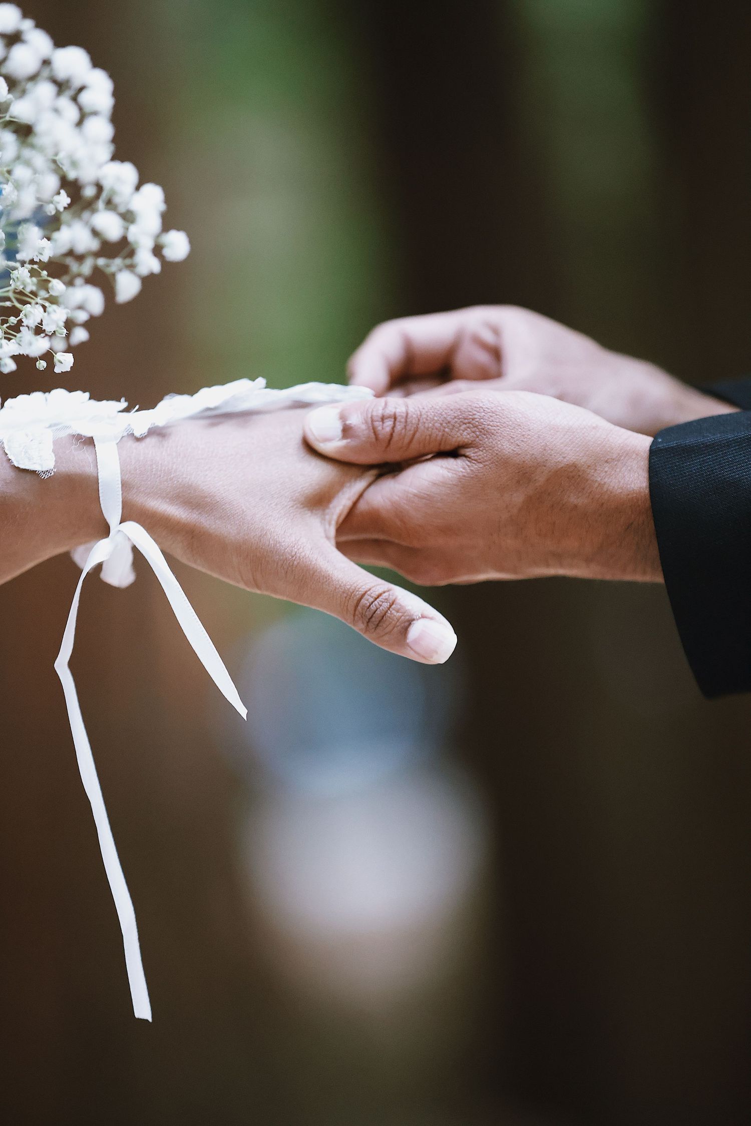 Close-up of groom placing wedding ring on bride's finger during outdoor ceremony with white floral bouquet.