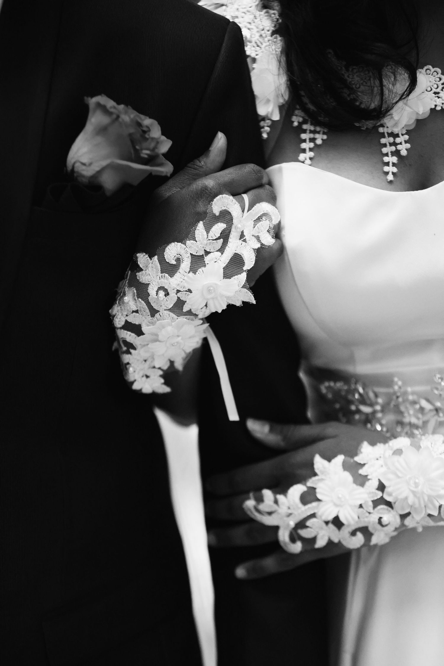 Black and white close-up of bride in lace sleeve wedding dress held by groom outdoors.