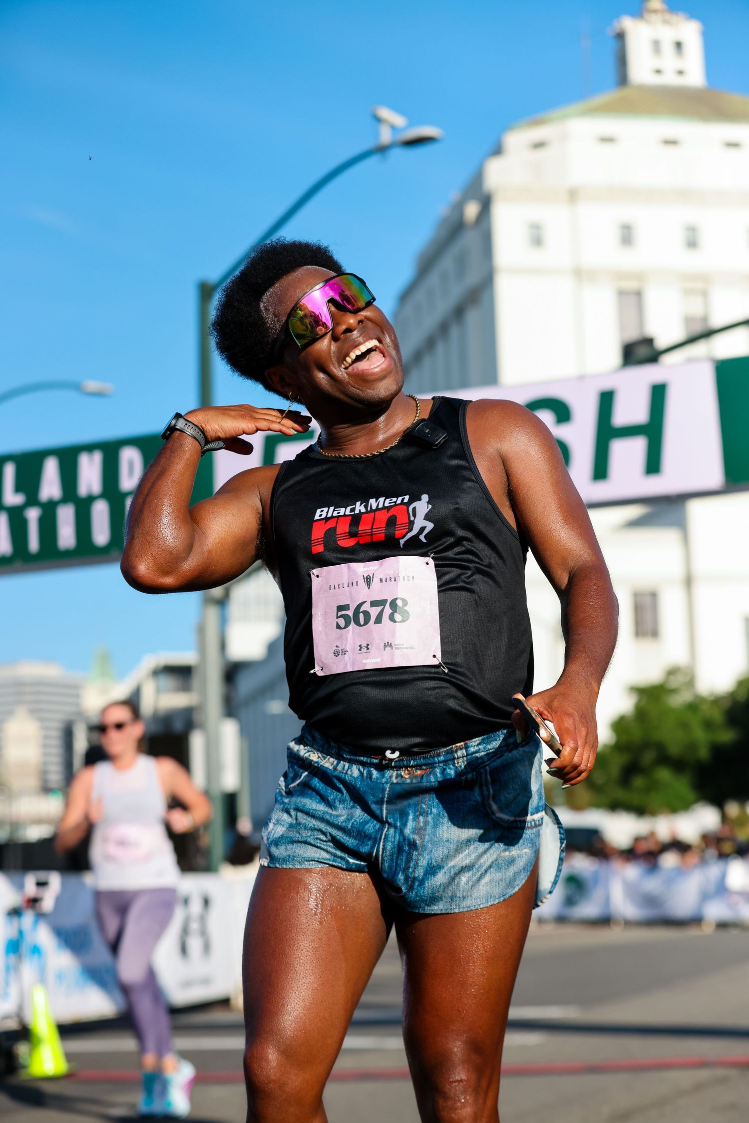 Joyful Black female runner wearing Black Men Run vest and bib 5678 celebrates at race finish line.
