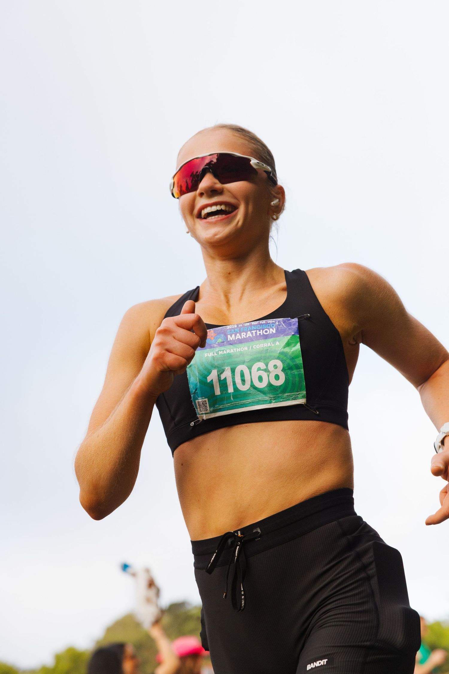 Smiling woman runner wearing bib number 11068 competing in a marathon race outdoors.