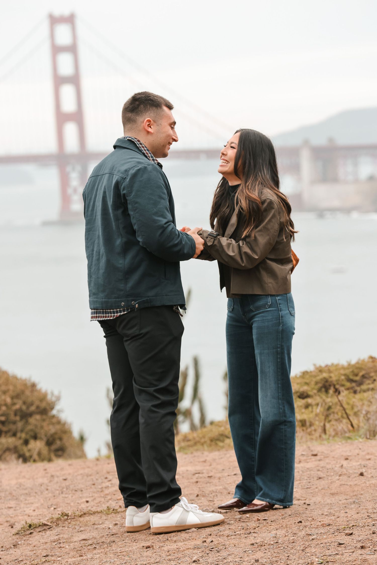 Couple holding hands and laughing together with Golden Gate Bridge backdrop.