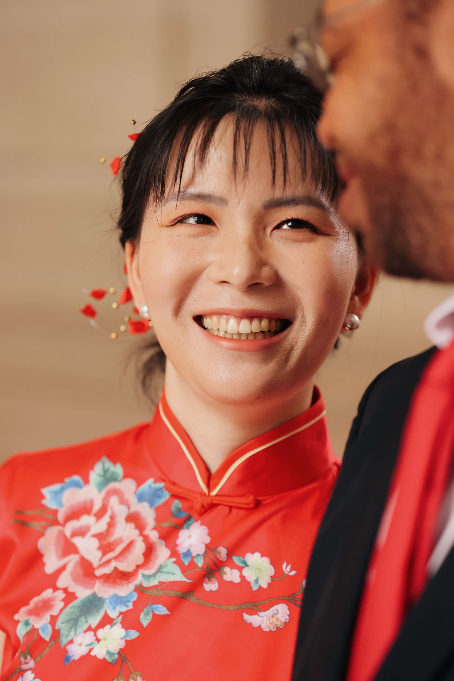 Smiling Asian bride in red floral qipao with hair accessories at wedding ceremony.