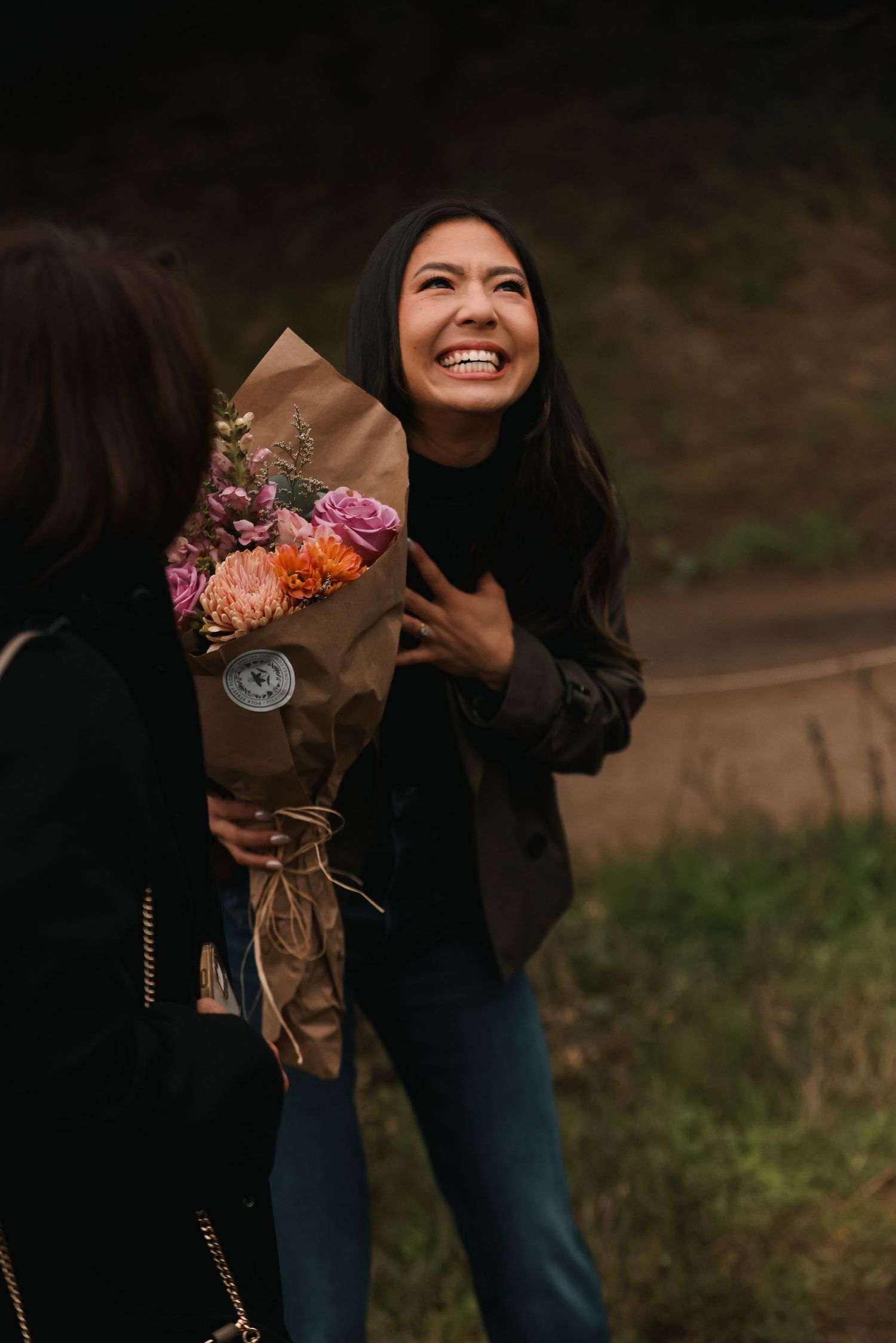 Joyful woman receiving bouquet of colorful flowers, laughing with delight outdoors.