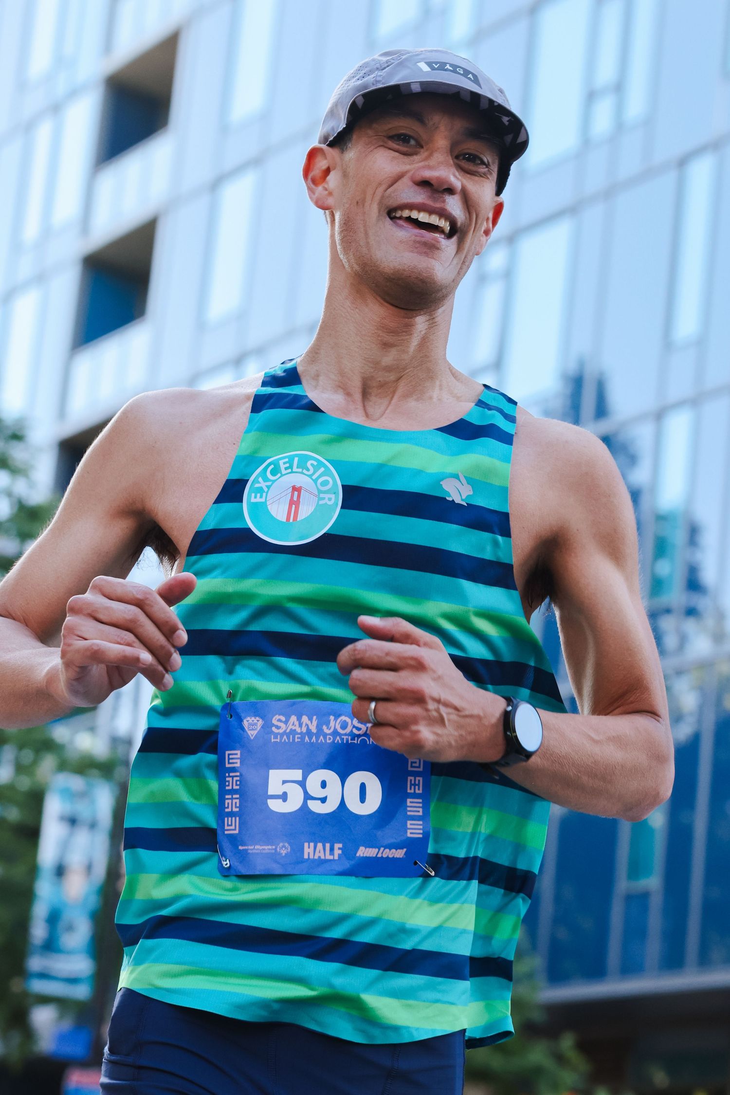 Smiling male runner wearing bib number 590 competes in San Jose Half Marathon in teal striped tank.