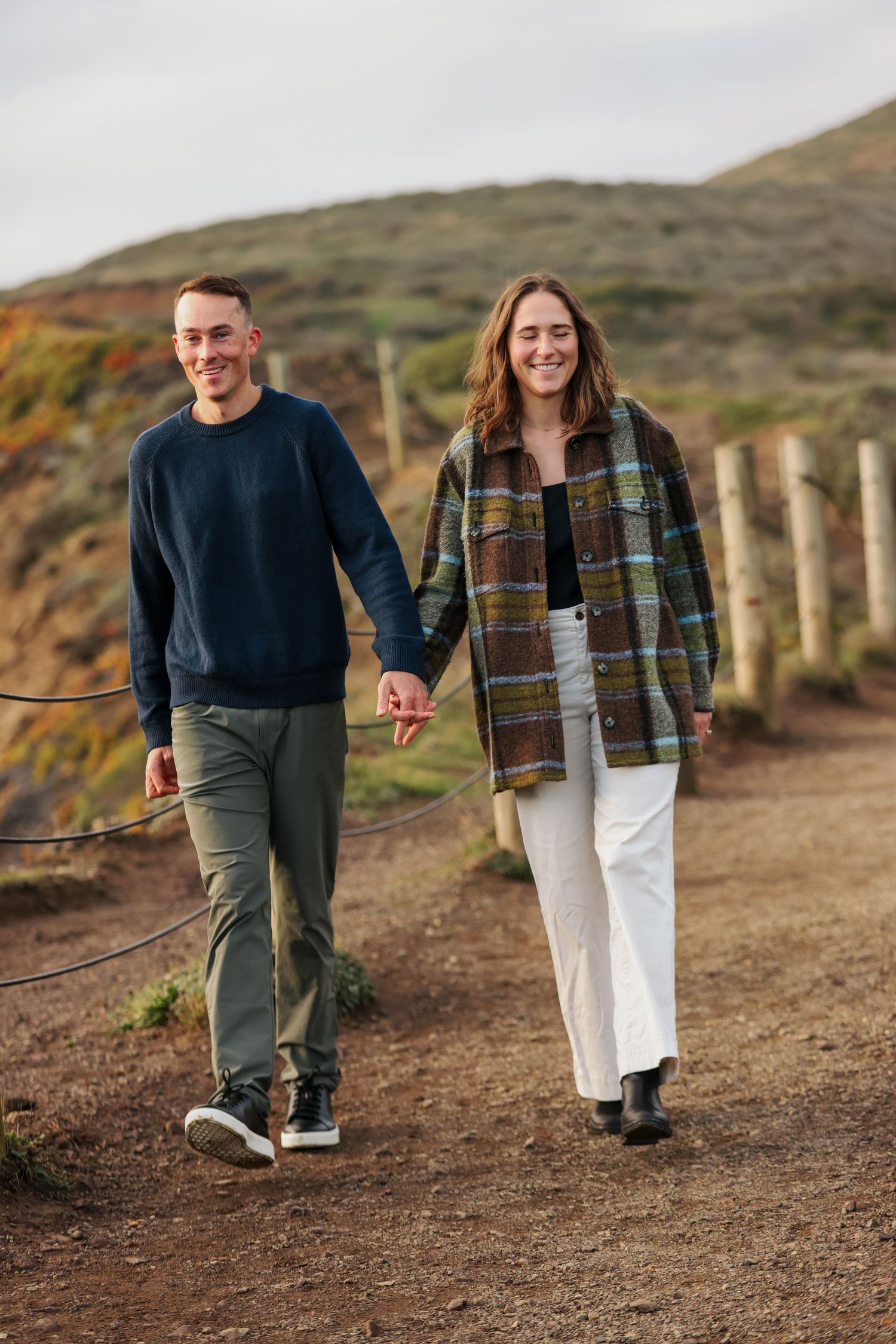Happy couple walking hand in hand along scenic coastal trail with hills.
