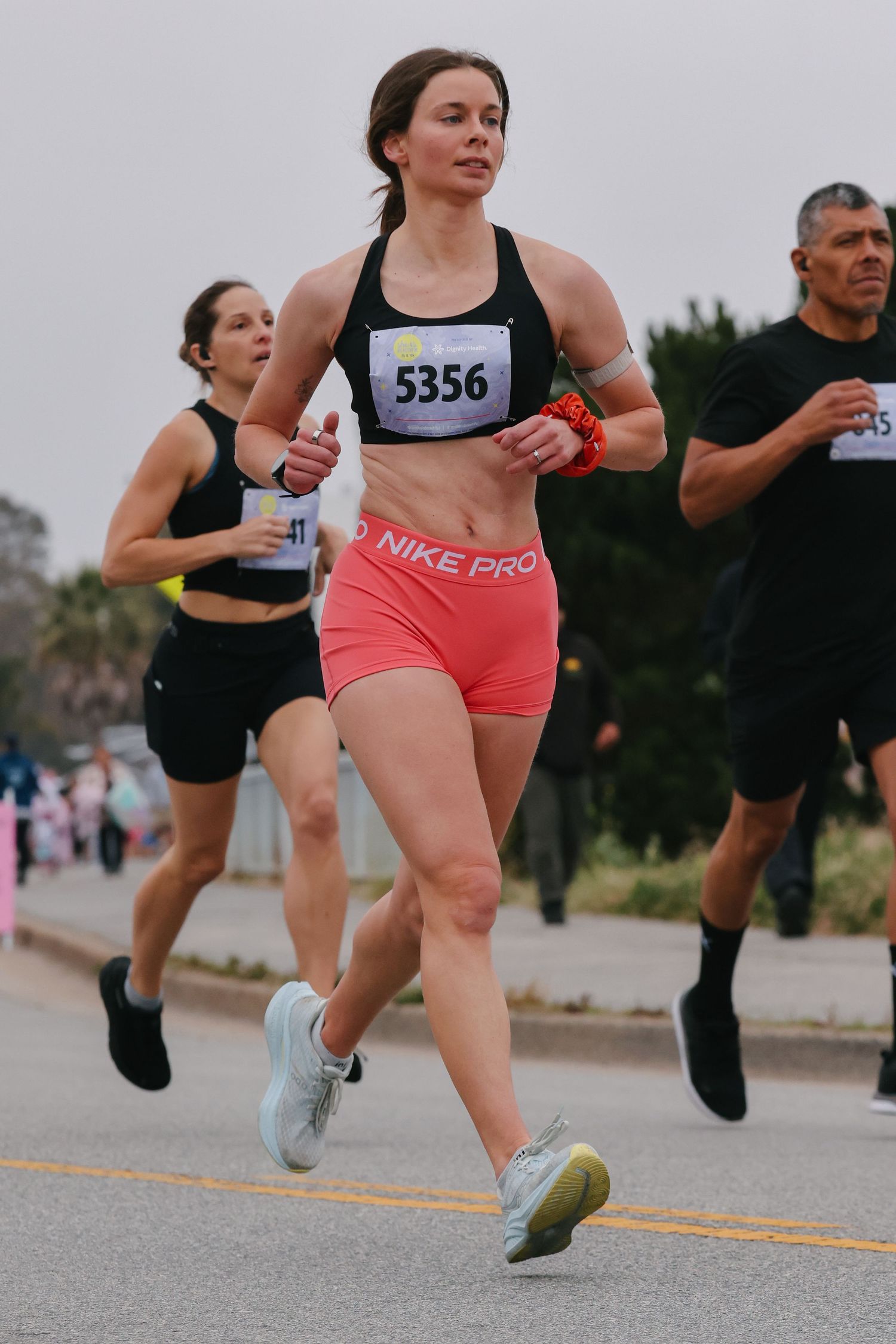 Female runner in Nike Pro pink shorts and black sports bra races with bib 5356 during a road race.