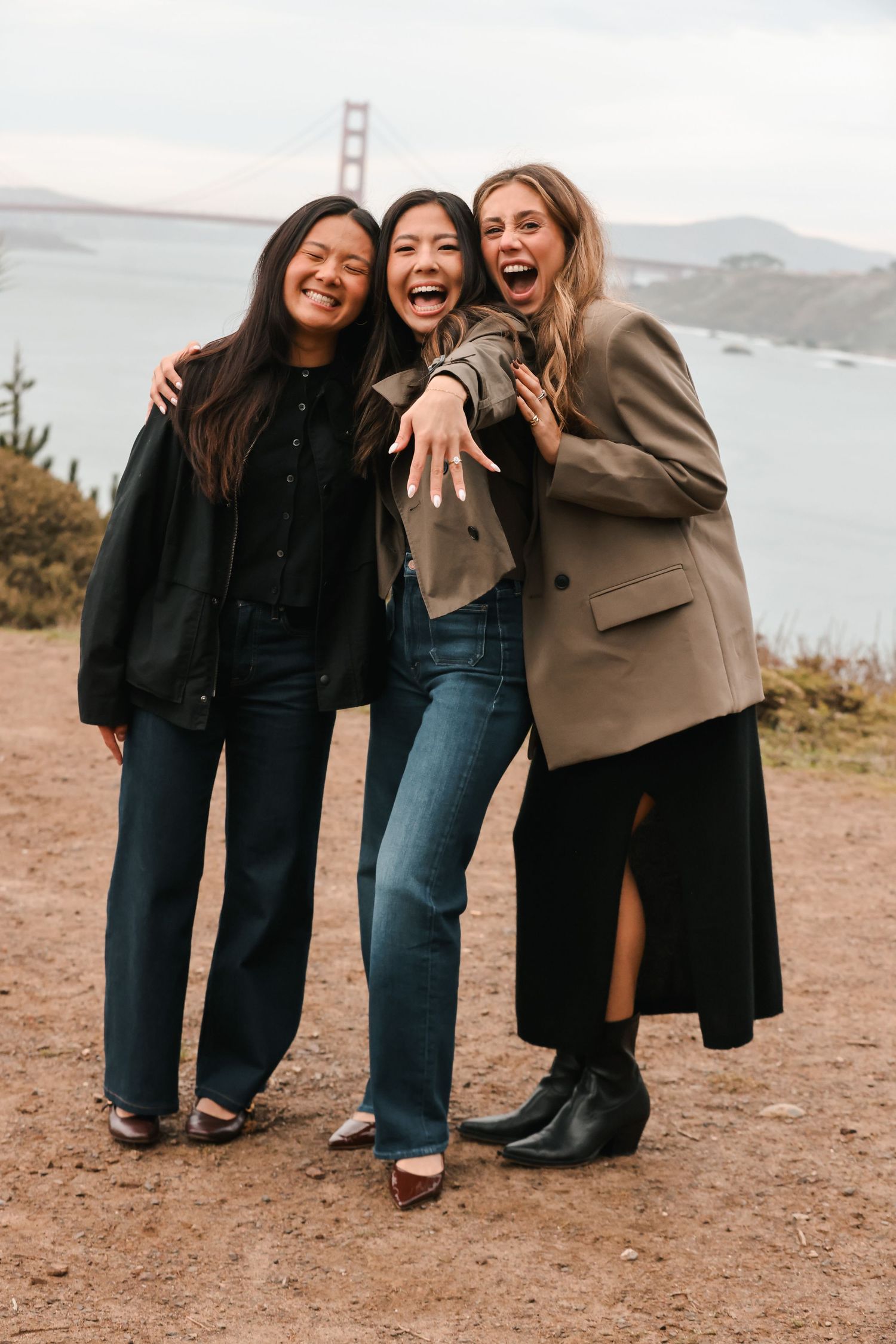 Three women celebrating engagement, showing ring near Golden Gate Bridge in San Francisco.