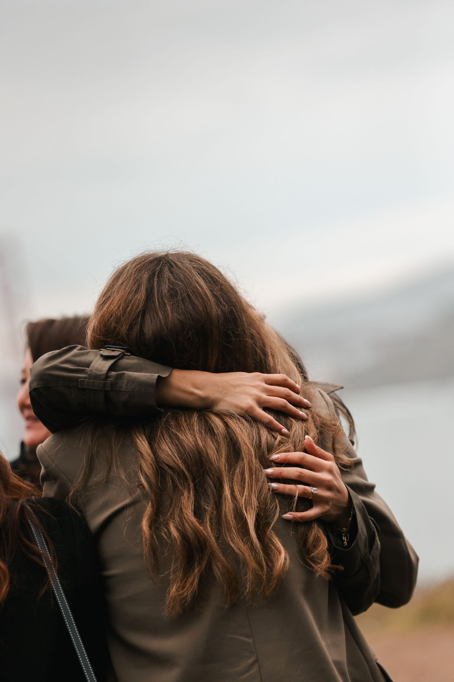 Two people sharing a warm embrace outdoors with overcast sky in background.