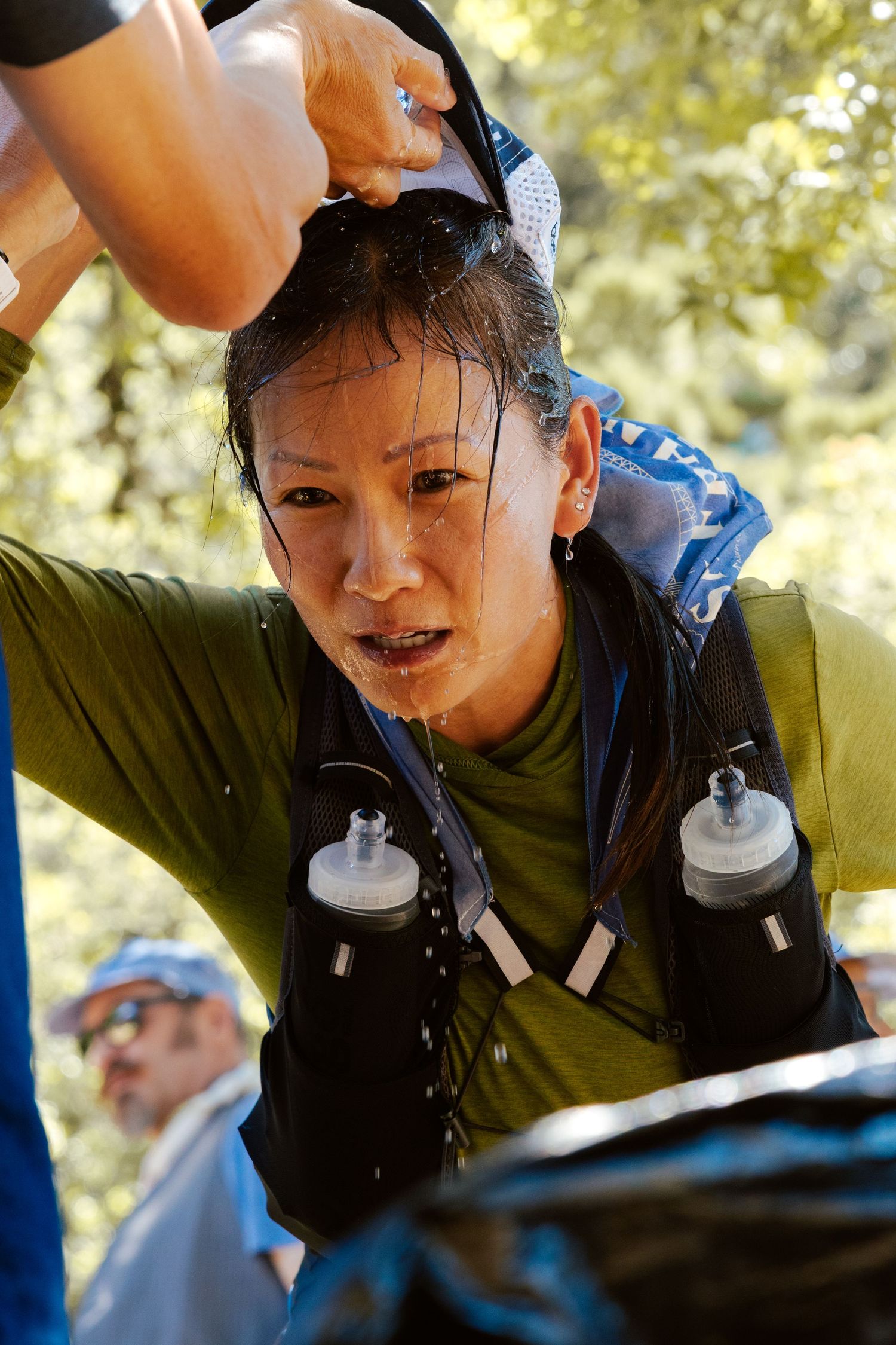 Exhausted female trail runner cools down by pouring water over her head during a hot race.