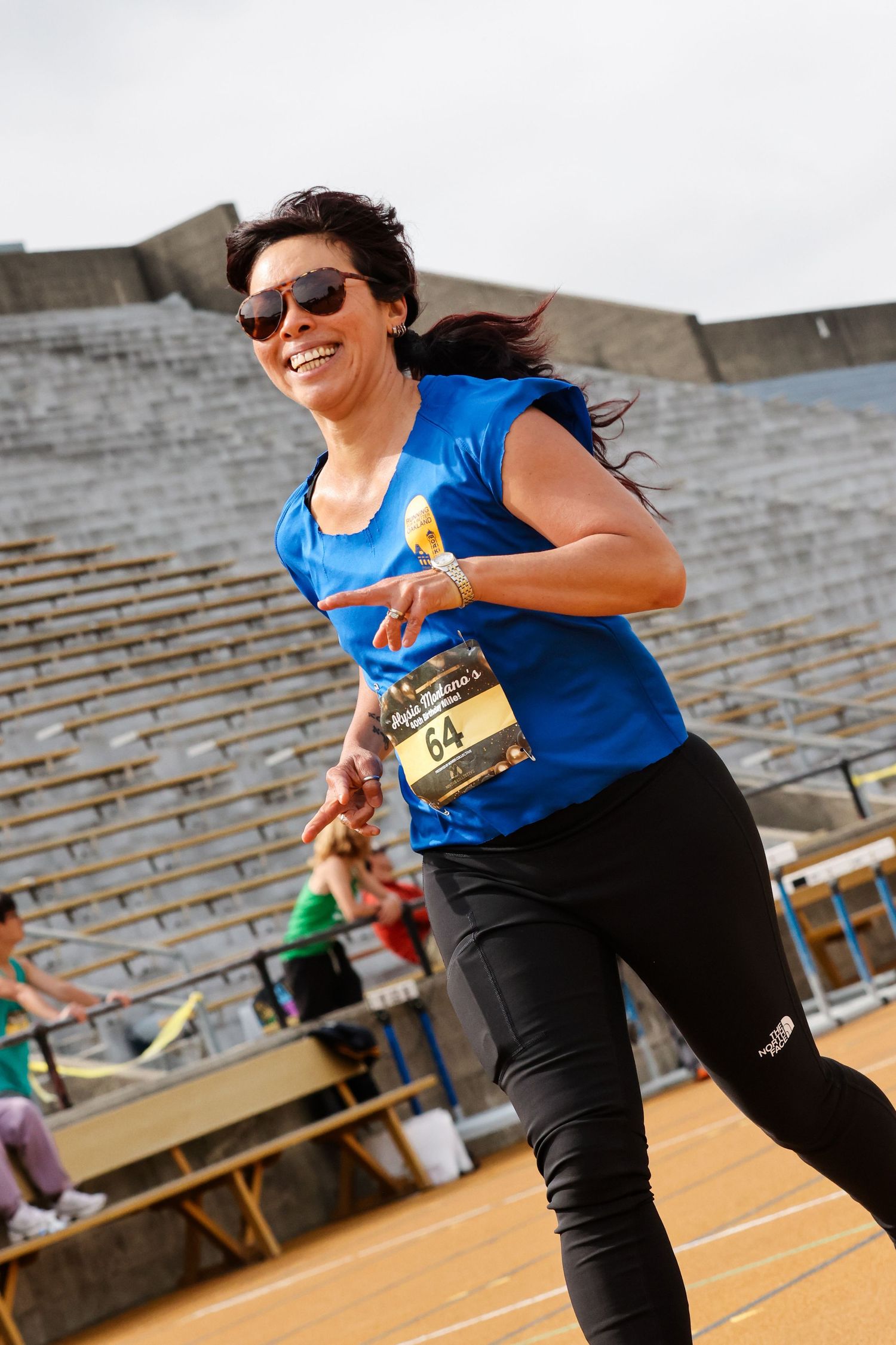 Smiling woman wearing bib 64 running in an outdoor stadium race event.