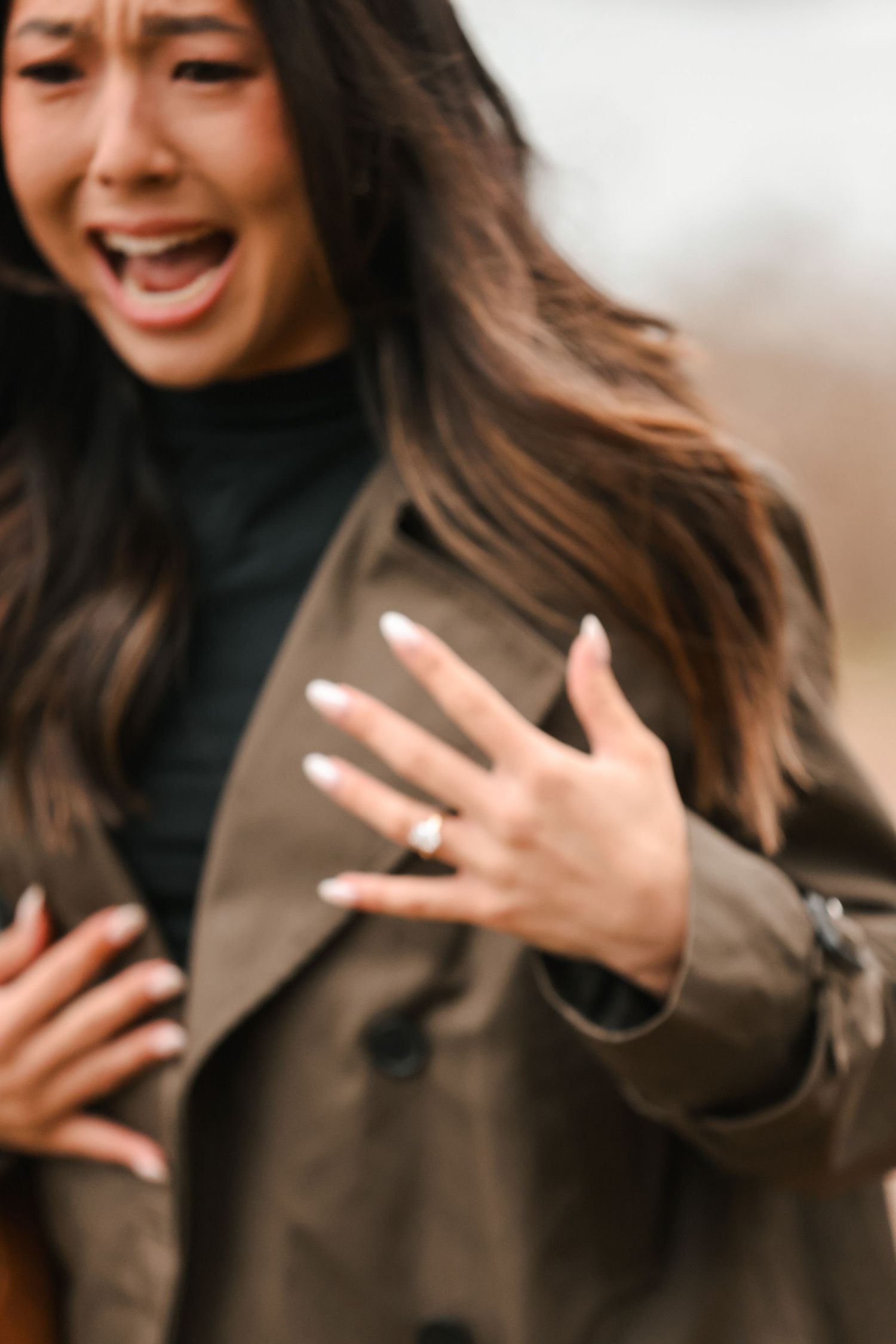 Emotional woman showing engagement ring while crying tears of joy outdoors.