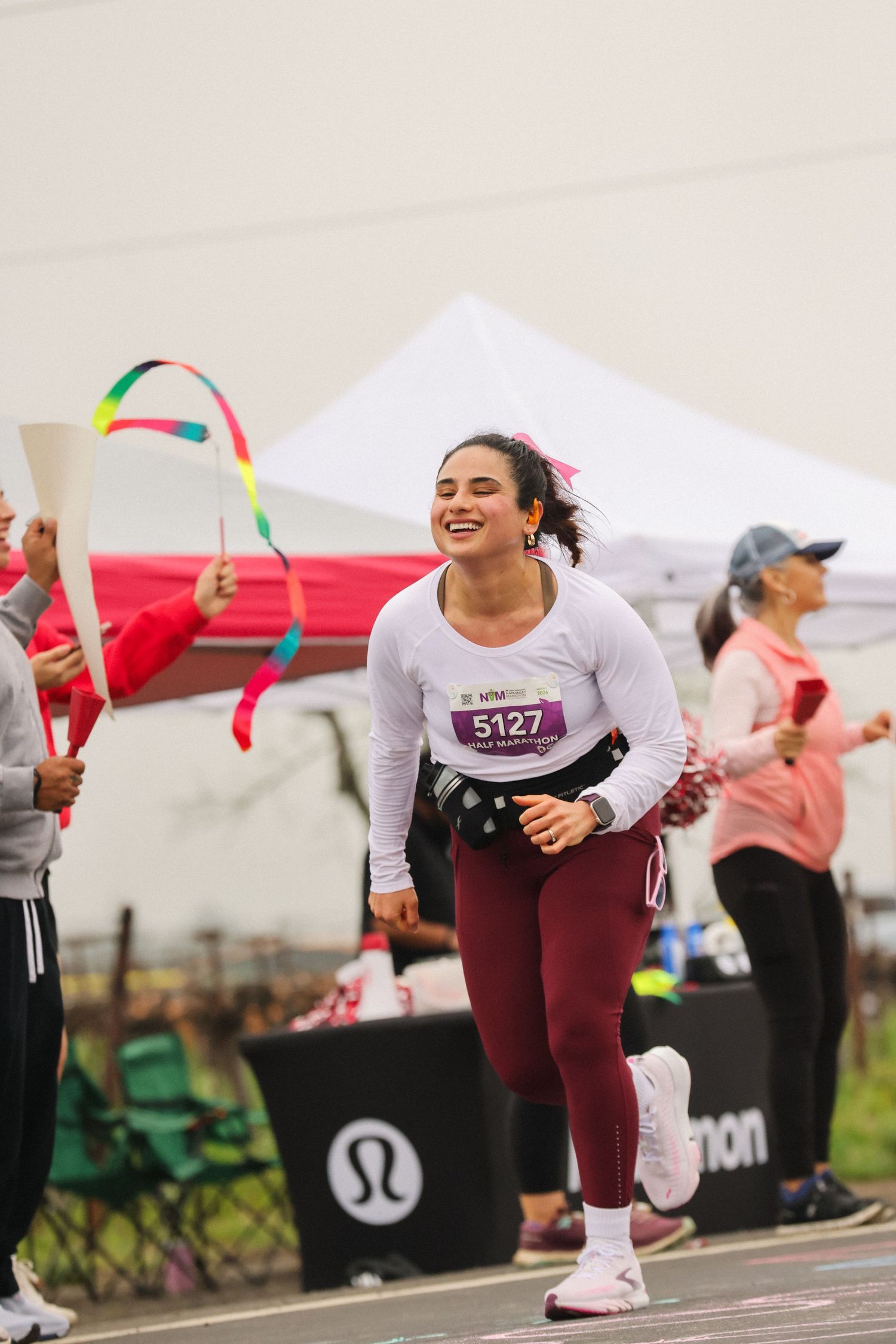 Happy female runner with bib 5127 smiles as she crosses the finish line at a lululemon sponsored race.