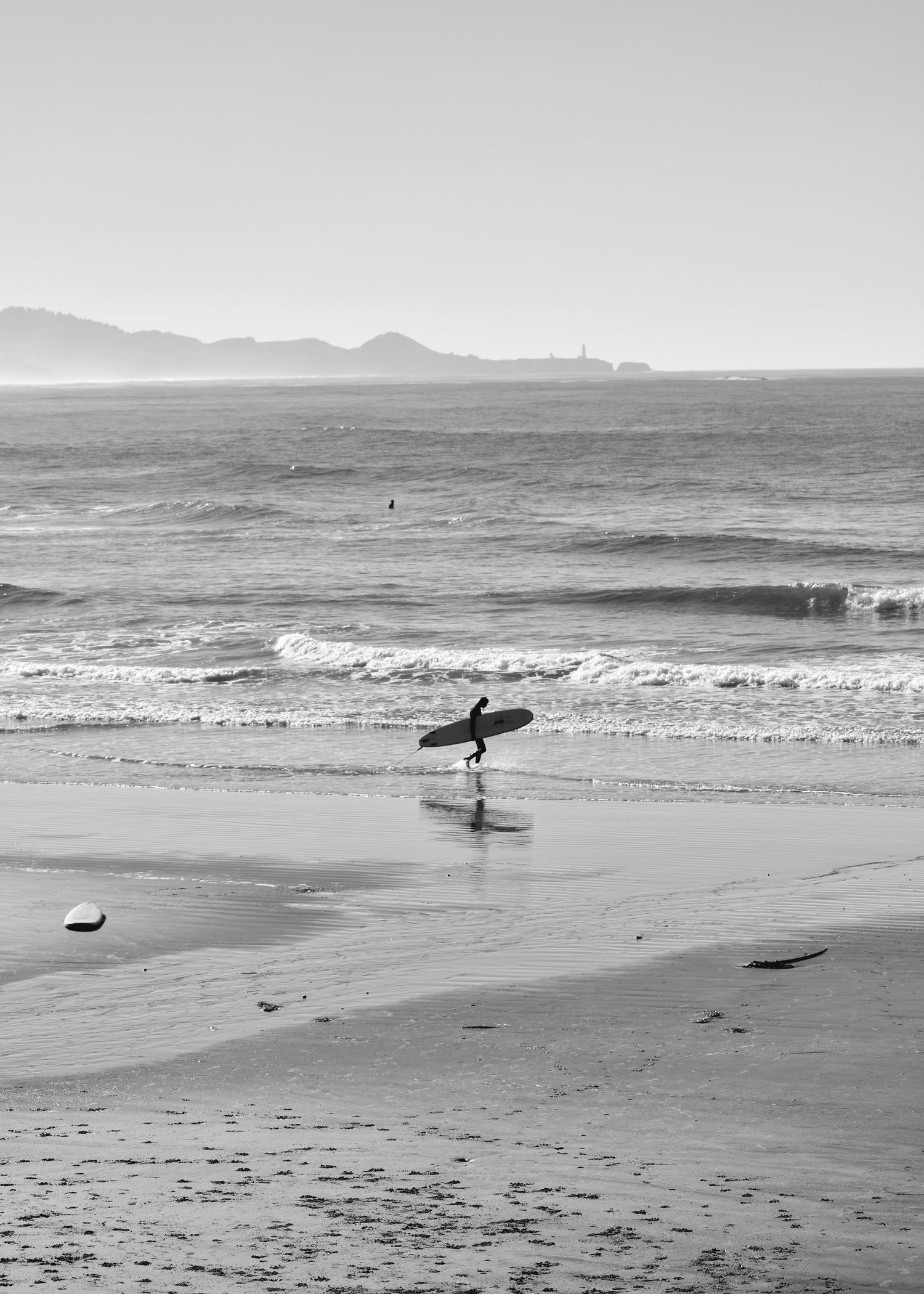 Black and white still image of surfer walking along beach in Newport Oregon.