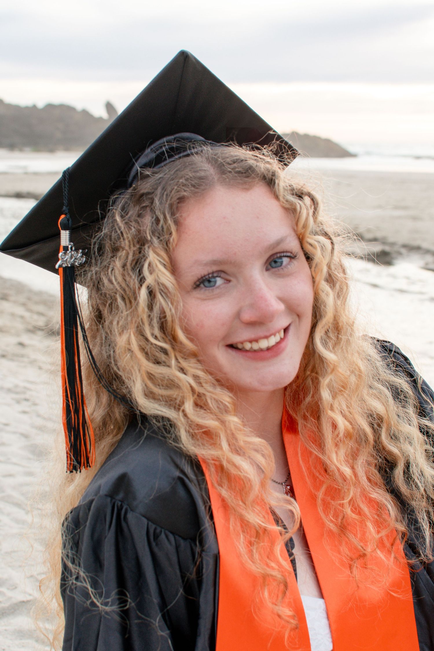 Female graduate wearing cap and gown during senior session at Fogarty Creek Beach in Oregon.