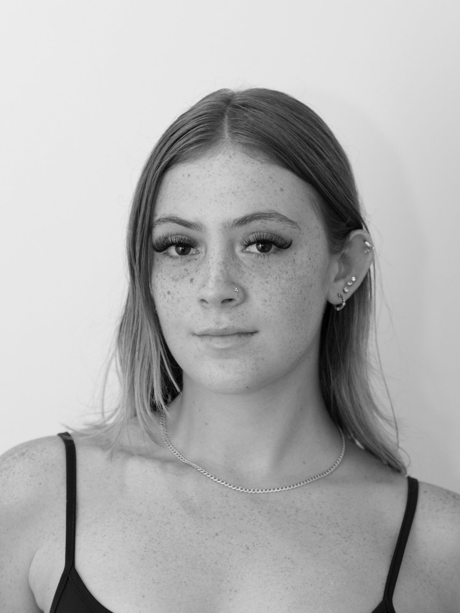 Black and white portrait of a young woman with freckles, long hair, earrings, and a delicate chain necklace.