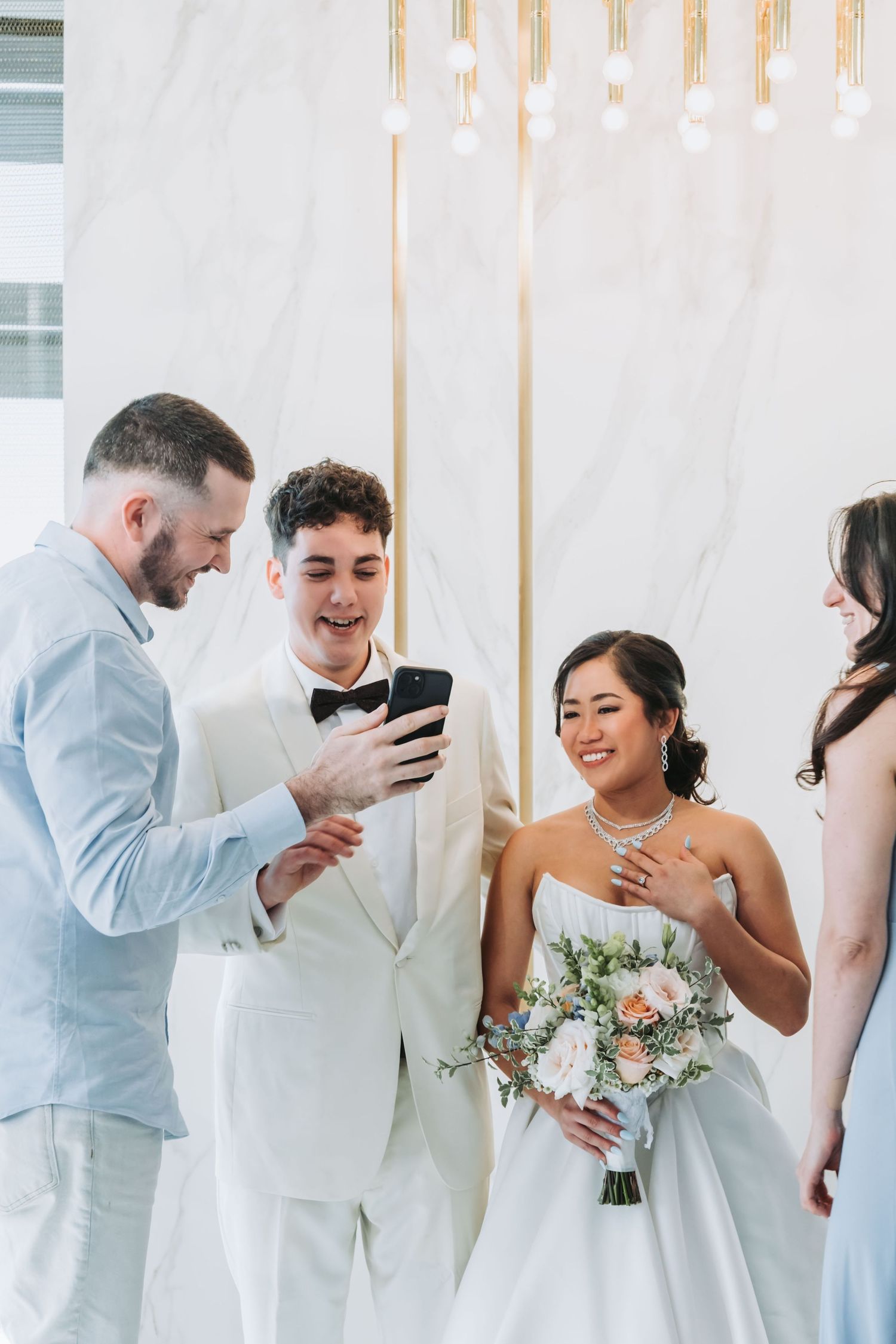 Bride and groom viewing phone with guests at elegant wedding reception venue.
