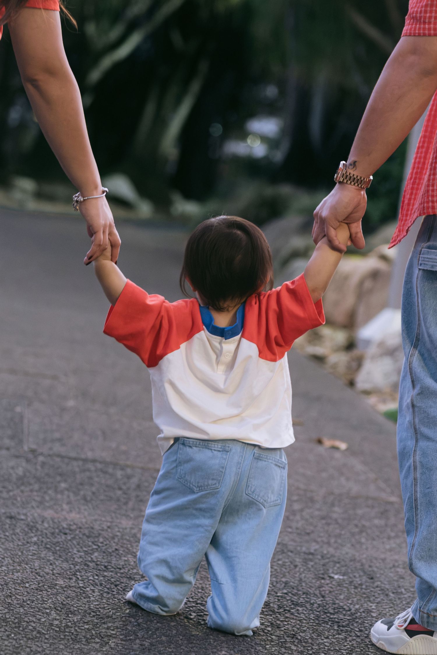 A candid shot of a toddler holding an adult's hands while walking.