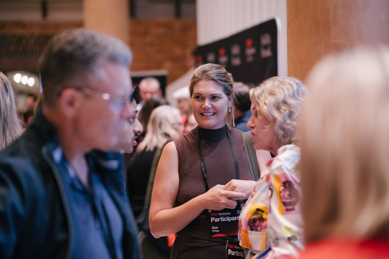A smiling woman wearing a participant badge mingles with guests at a professional networking event indoors.