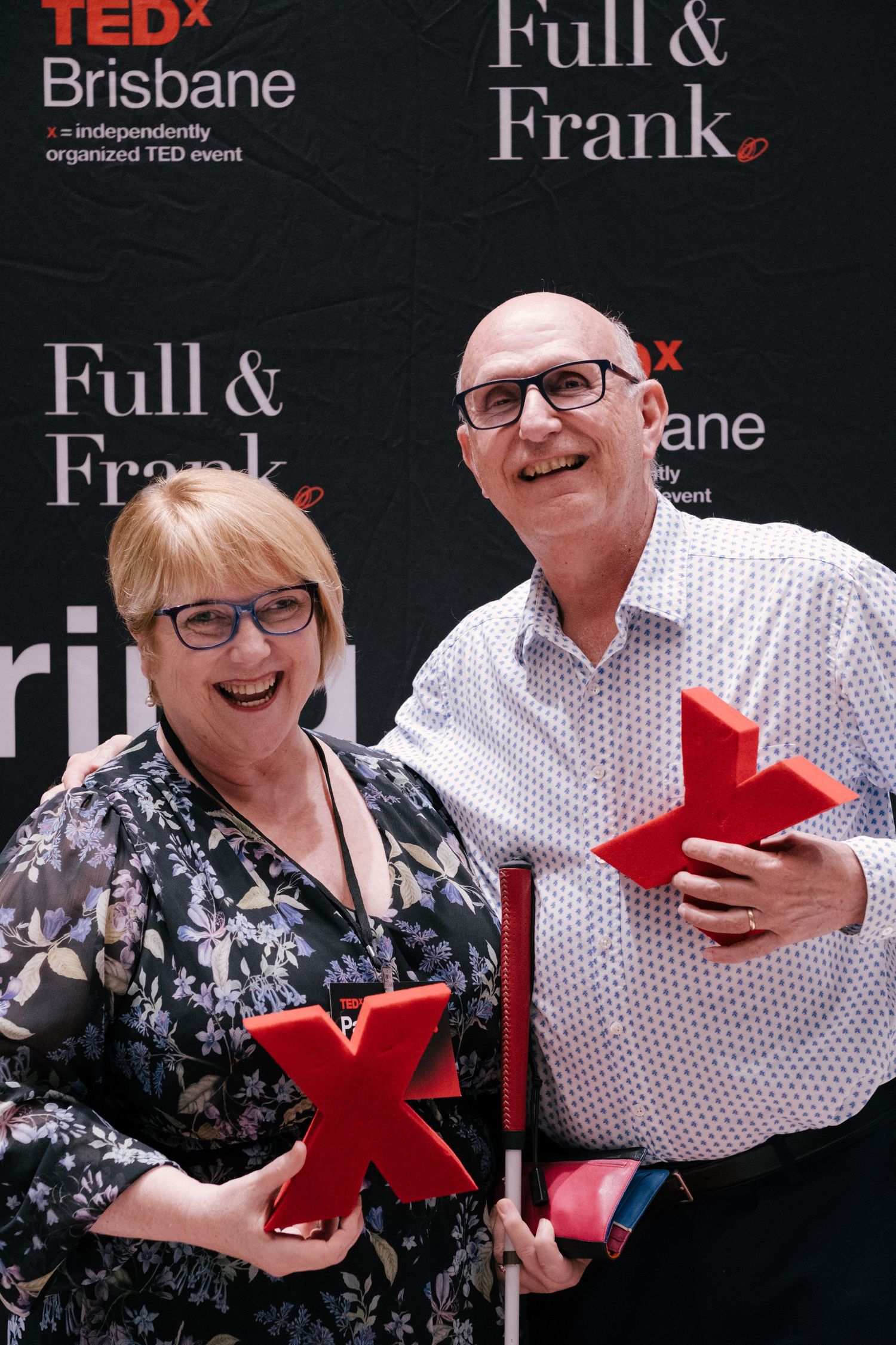Two smiling attendees pose with red TEDx trophies at TEDx Brisbane event, sponsored by Full & Frank.