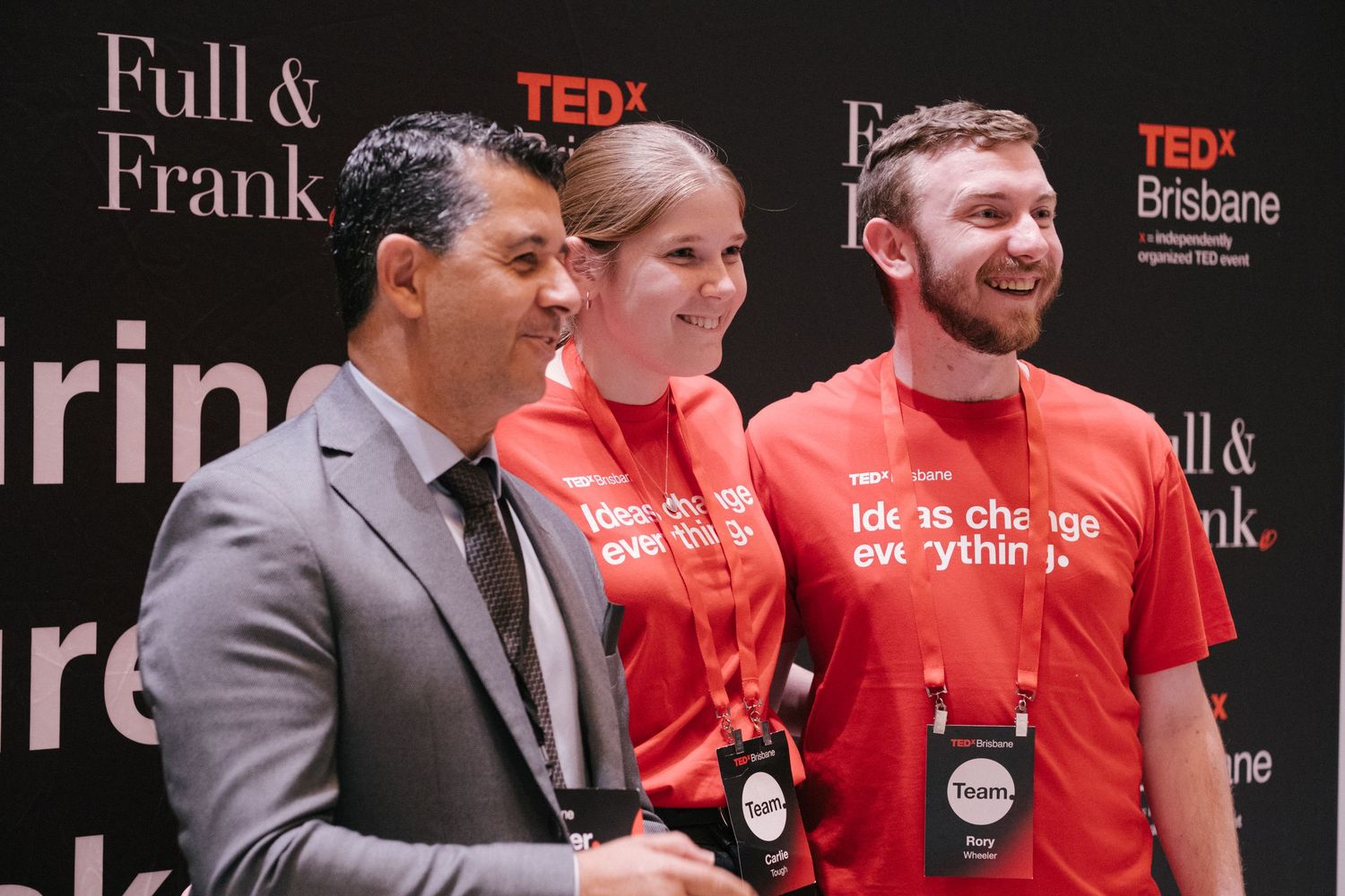Three people smiling at TEDx Brisbane event, two wearing red Ideas Change Everything shirts.