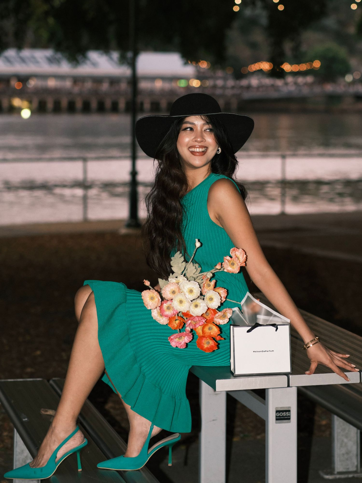 A woman wearing a green dress and hat, posing and smiling on a bench.