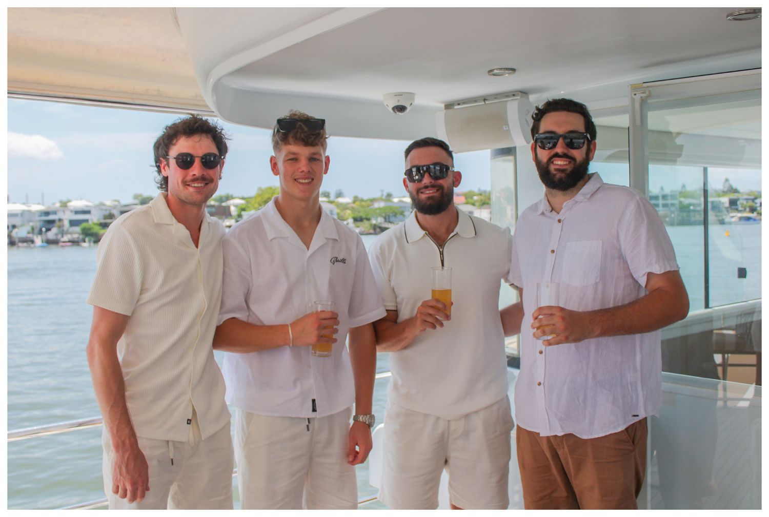 Four men standing and posing together with drinks on a boat.