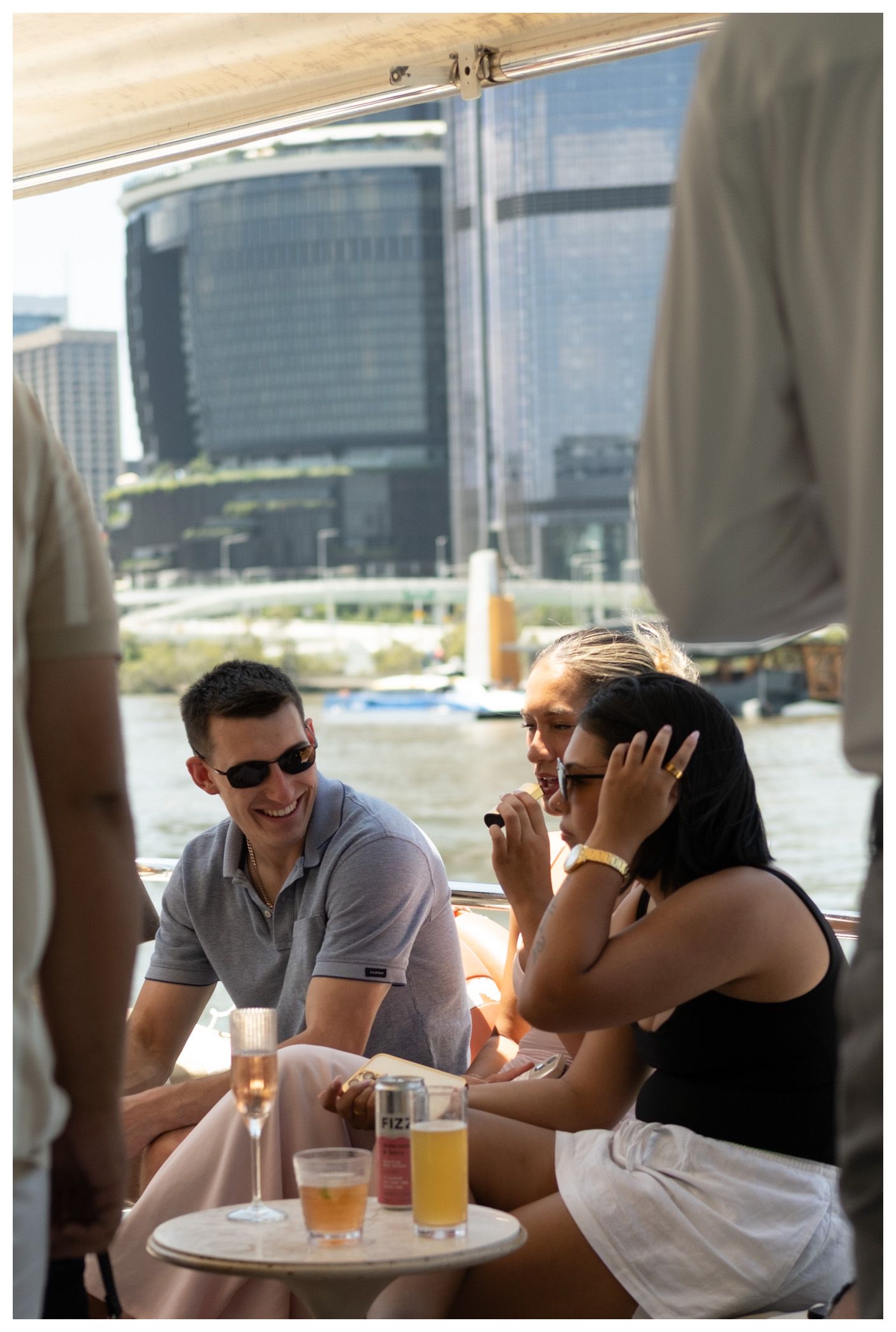 Friends enjoying drinks on a boat cruise with city skyline views on a sunny day.