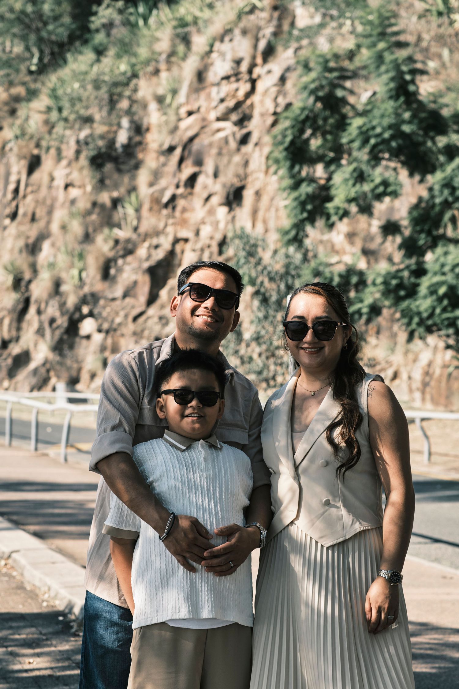 A family of three posing for a photo against a rock wall outdoors.
