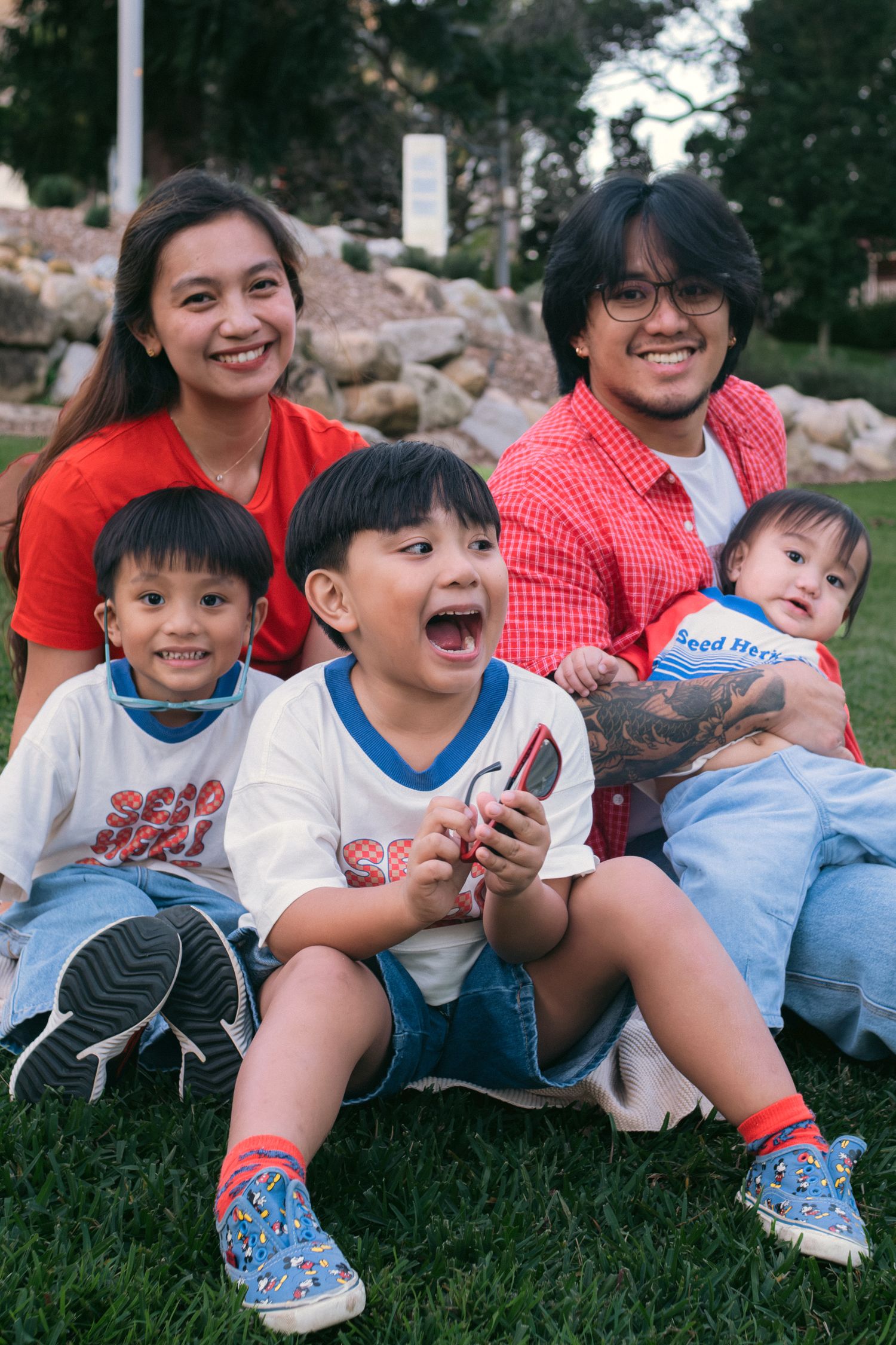 A family of four sitting on grass and laughing together.