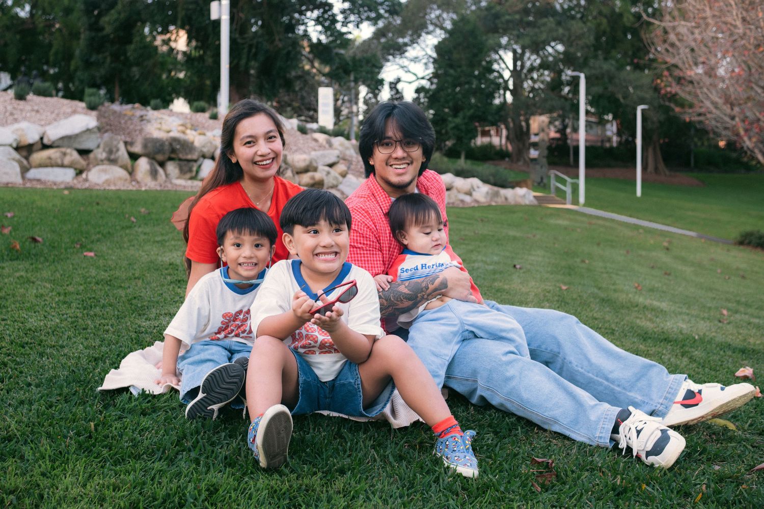 Happy Asian family of five smiling together on green grass in a park on a sunny day.