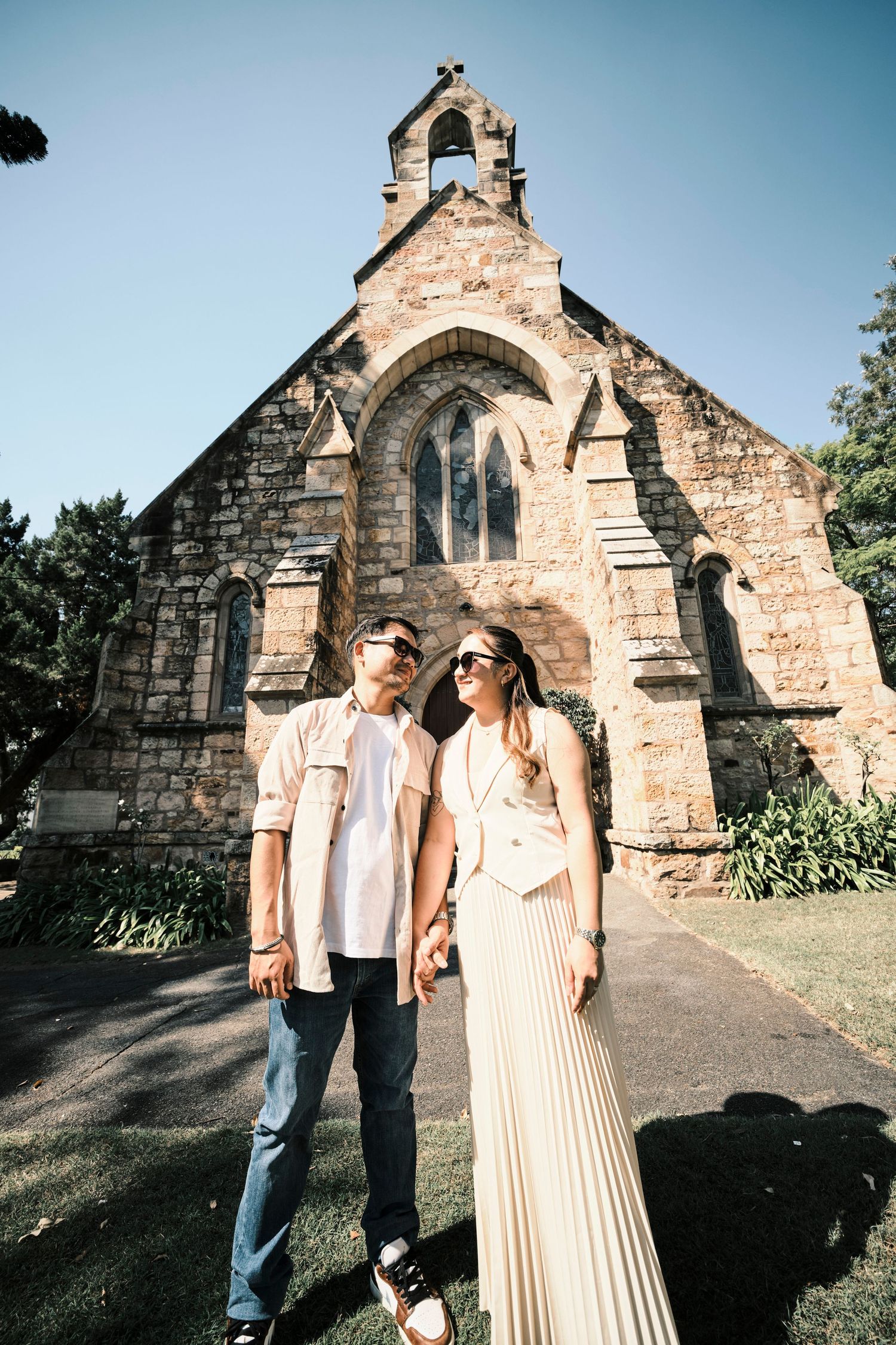 A couple posing in front of a stone church building.