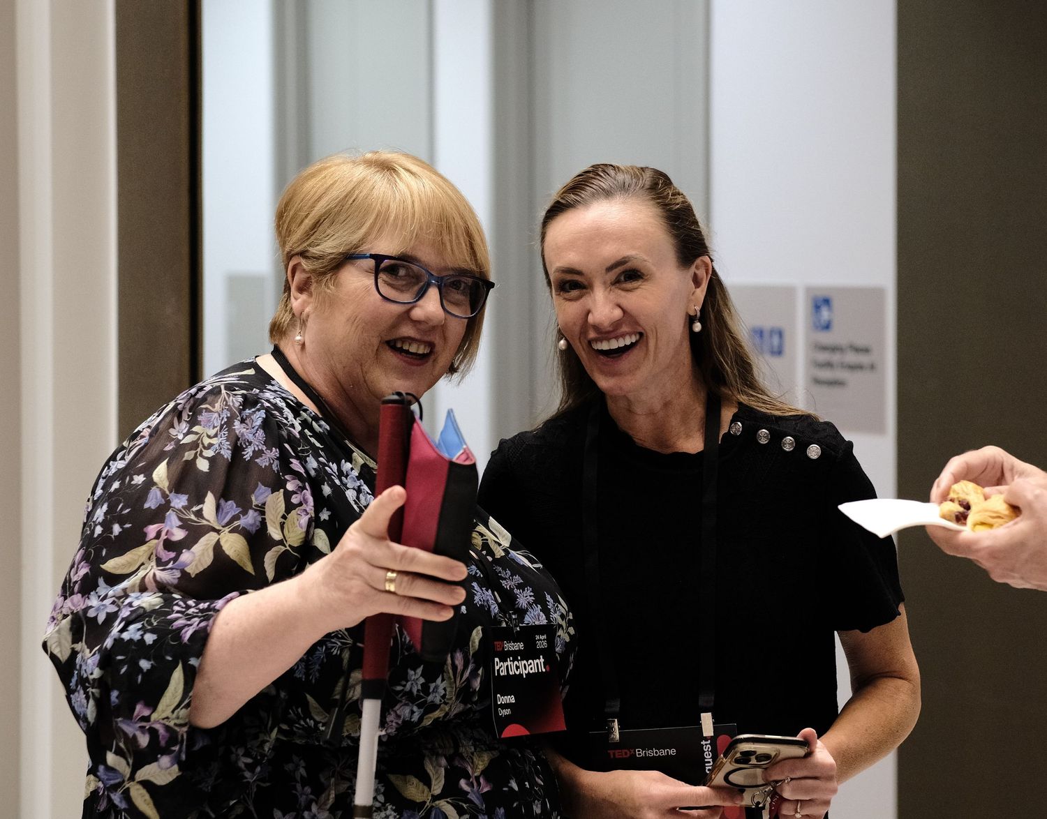 Two women conversing and smiling while holding event badges at TEDxBrisbane.