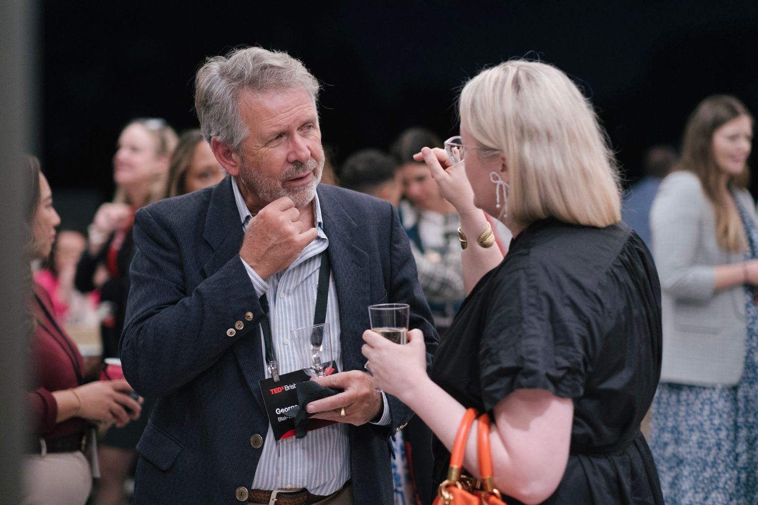 Two professionals networking at a conference event, engaging in conversation while holding drinks indoors.