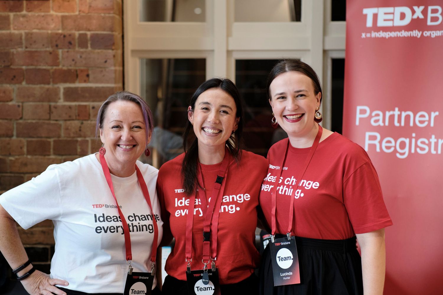 Three women smiling and posing in front of a TEDx event sign.