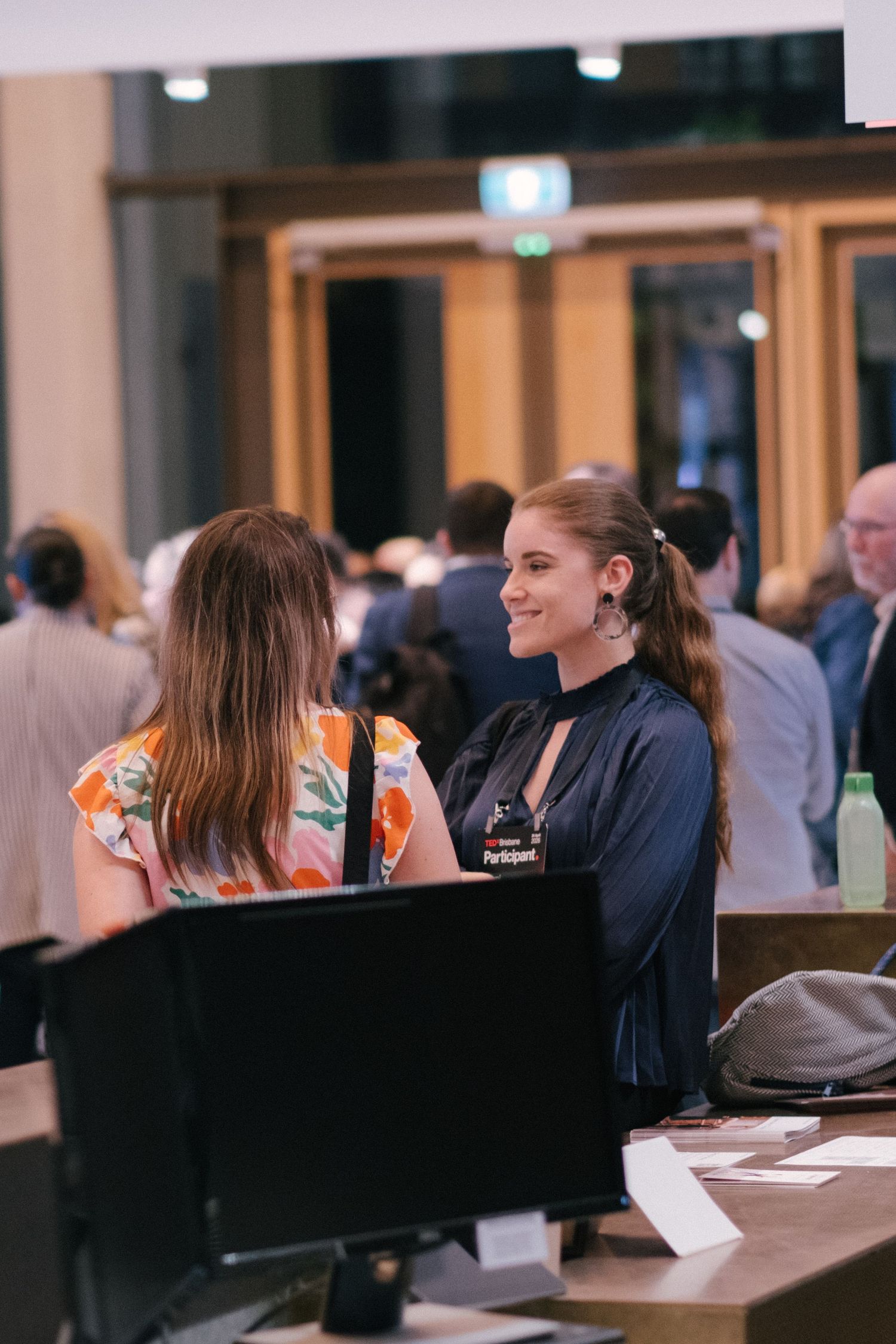 Smiling woman at registration desk welcoming attendee at a professional conference event.
