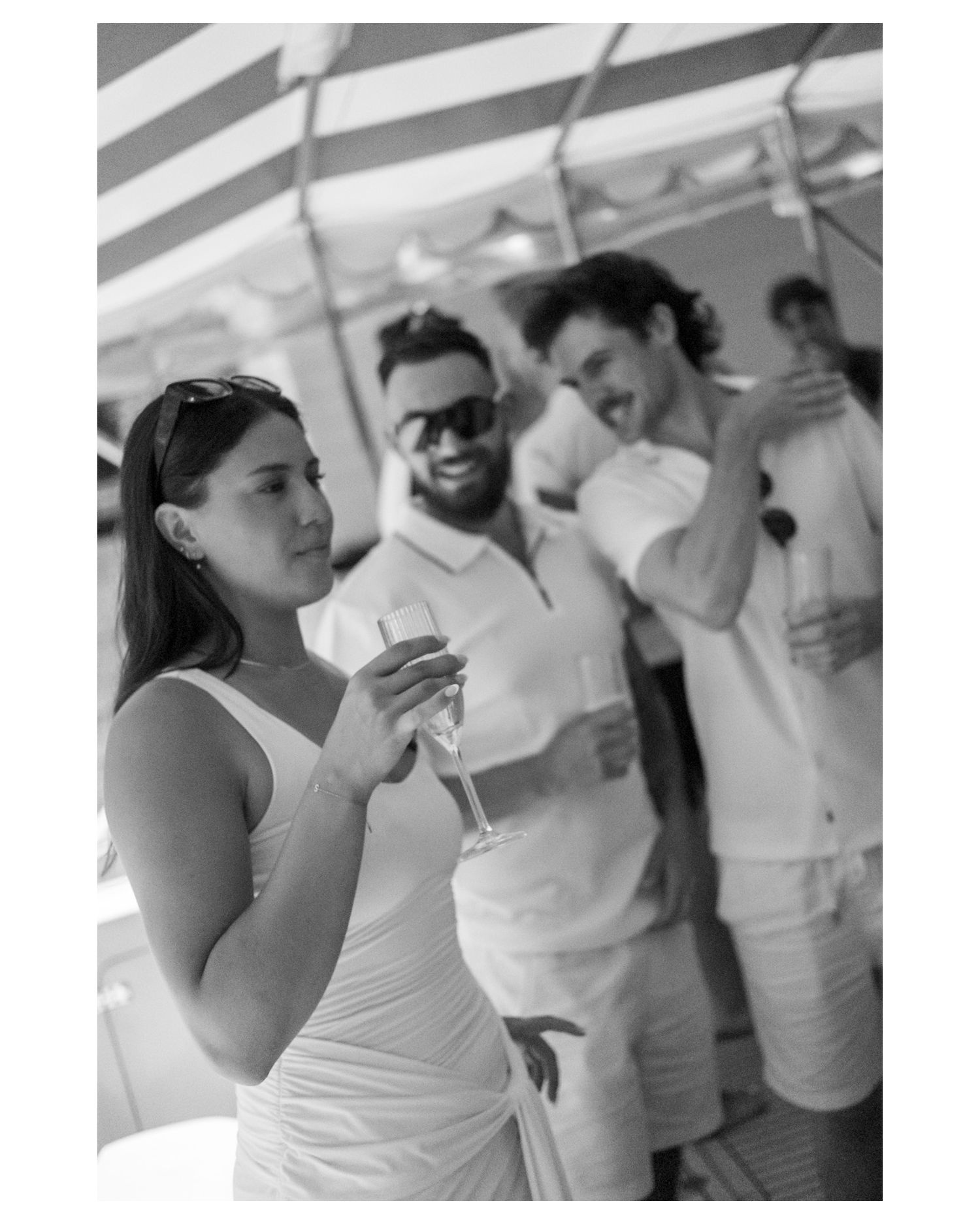 Black and white photo of elegantly dressed guests in white attire enjoying champagne at an outdoor summer party.