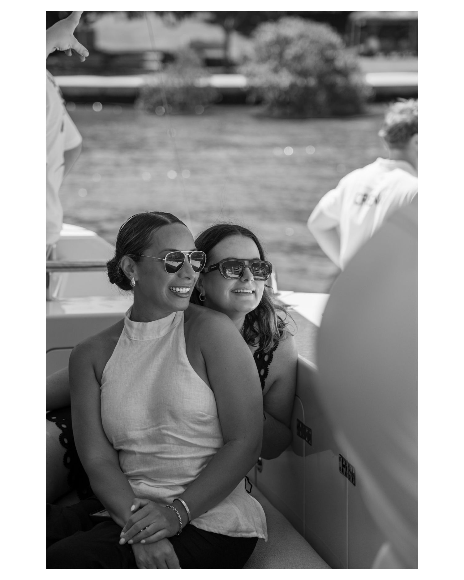 Two women wearing sunglasses smile while seated on a boat, enjoying a sunny day on the water in black and white photo.