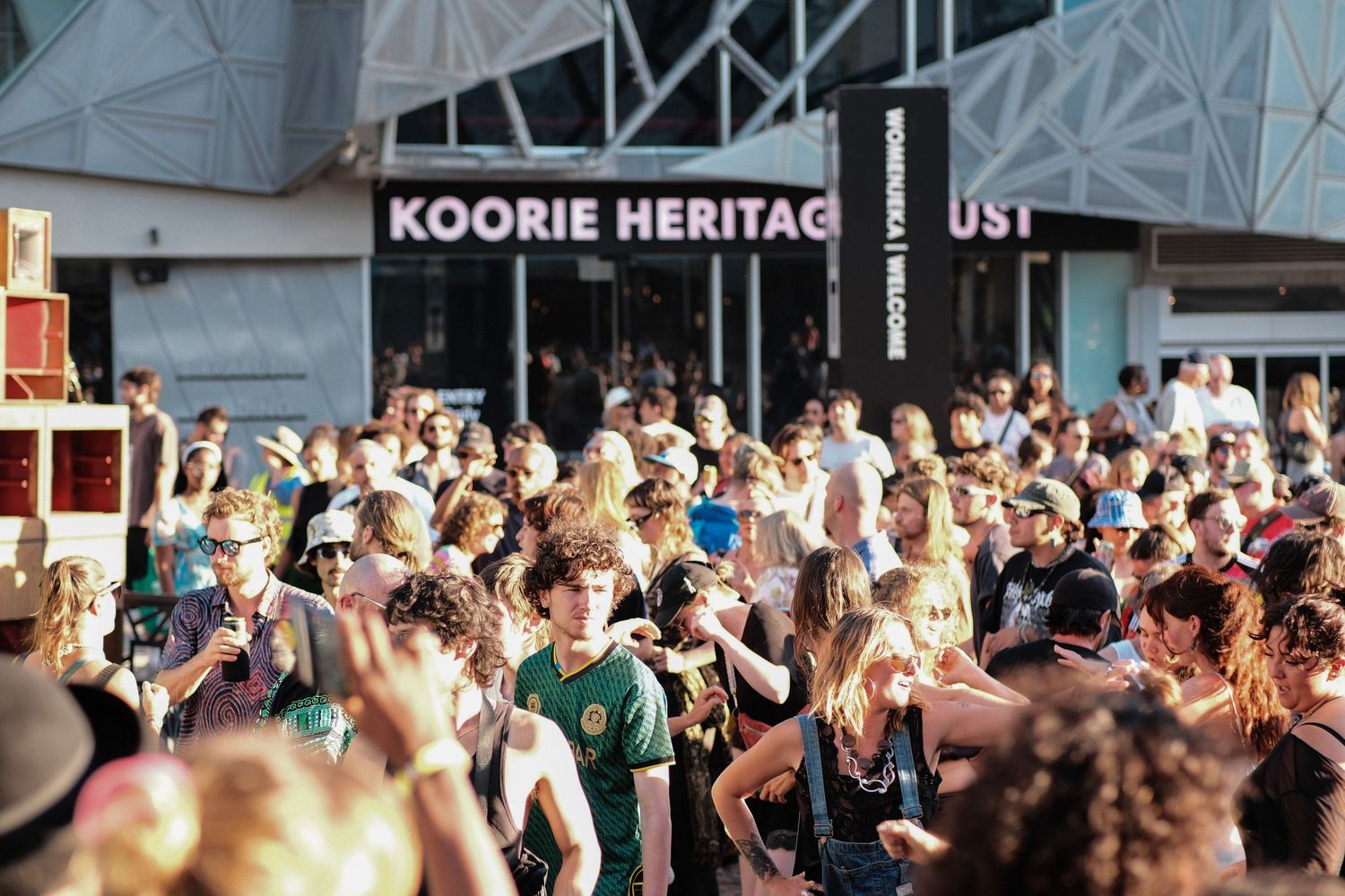 Large crowd gathered at outdoor festival near Koorie Heritage Trust building.
