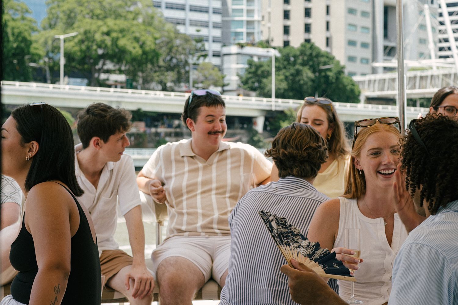 Group of young adults laughing and socializing outdoors in an urban setting on a sunny day.